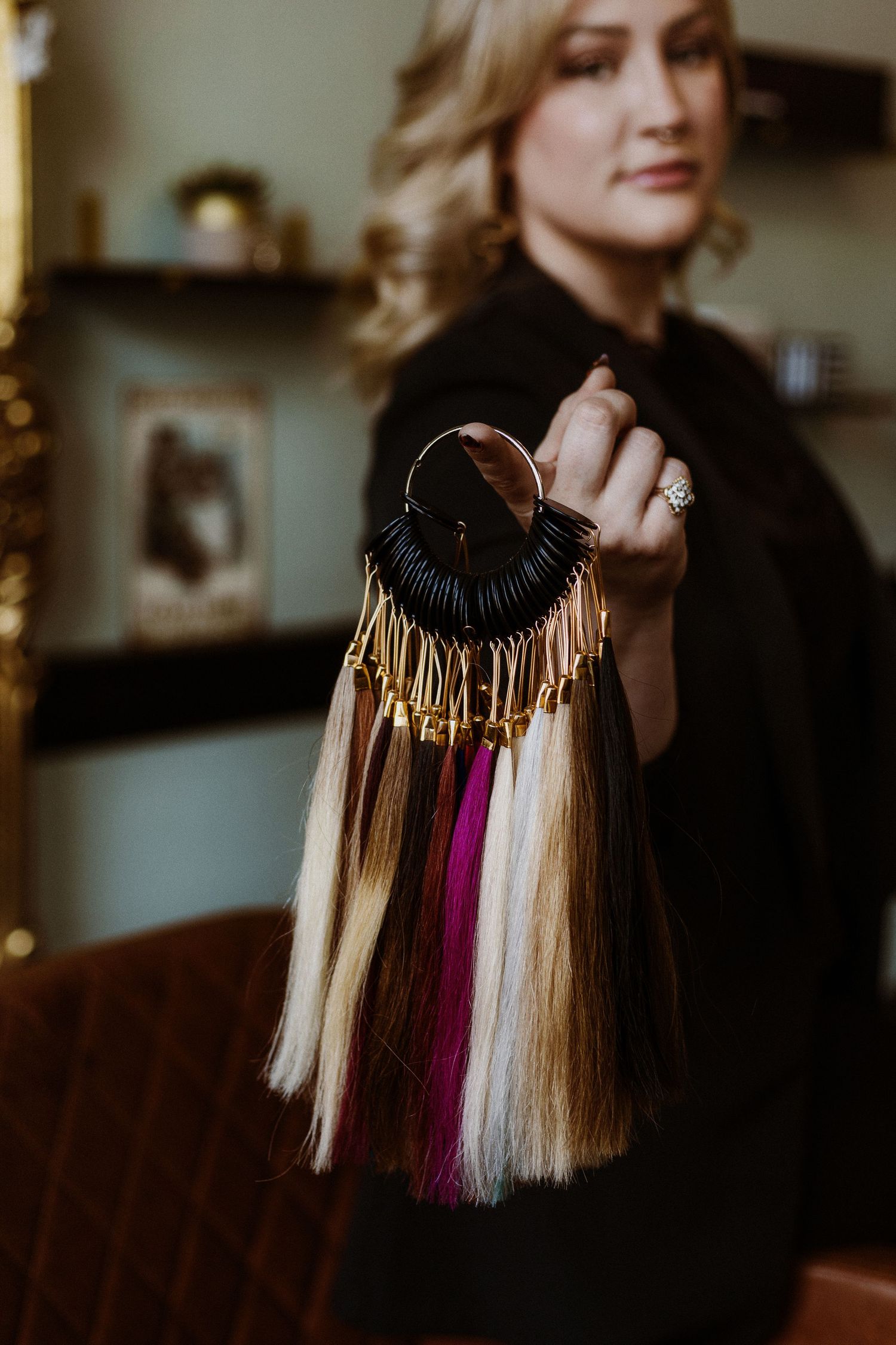 A hand holds a display of hair color swatches featuring blonde, pink and light tones against a dark background.