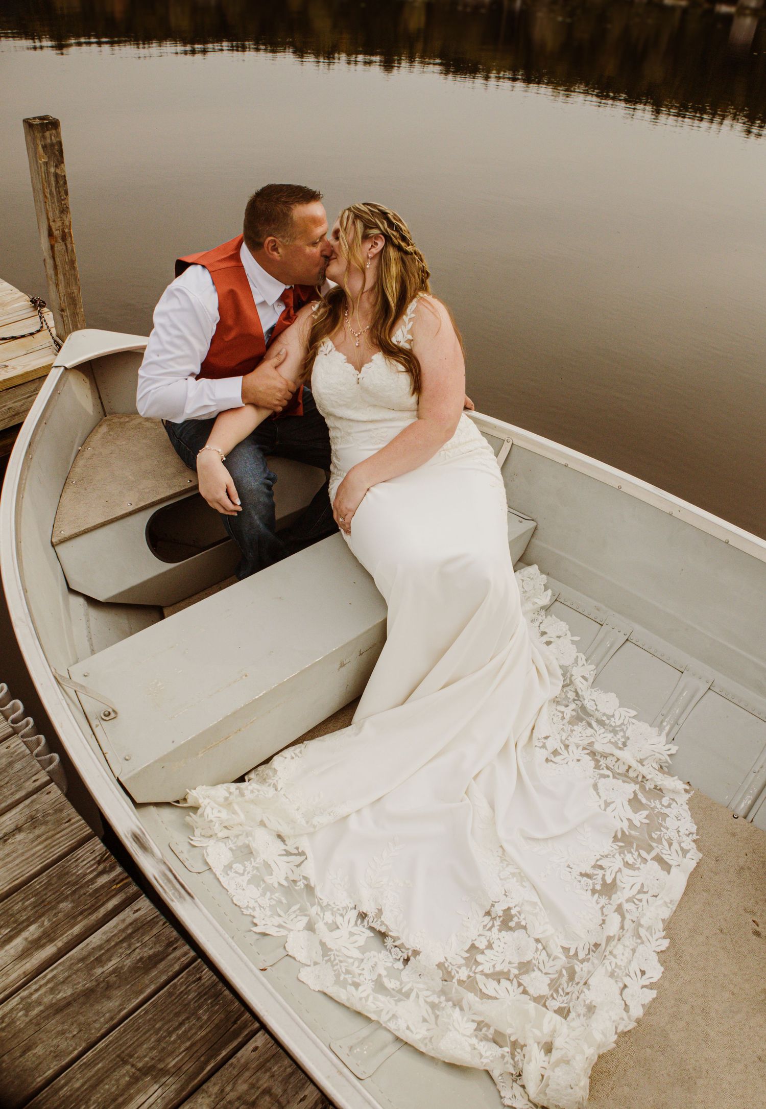 A romantic moment captured in a rowboat with a flowing white wedding dress trailing across the wooden seats.