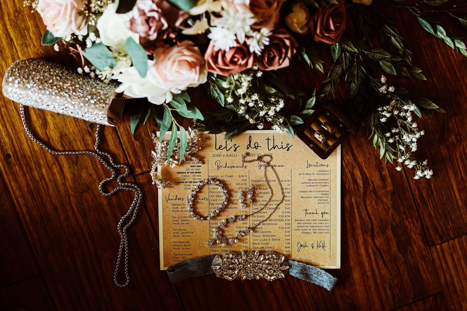 Wedding details flat lay with flowers and vintage-style paper on wooden surface.