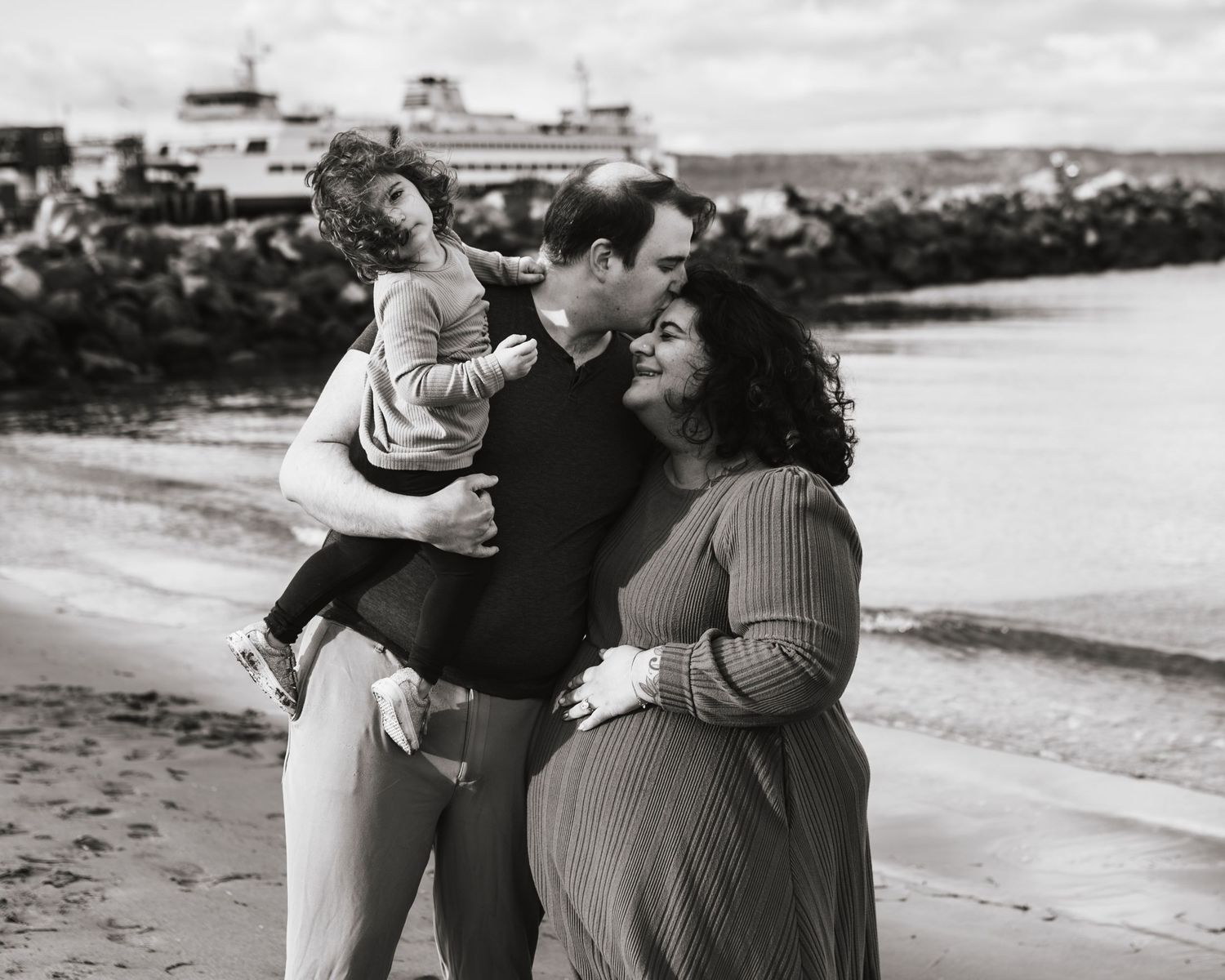family of three cuddled up and happy on the beach in Mukilteo during maternity session
