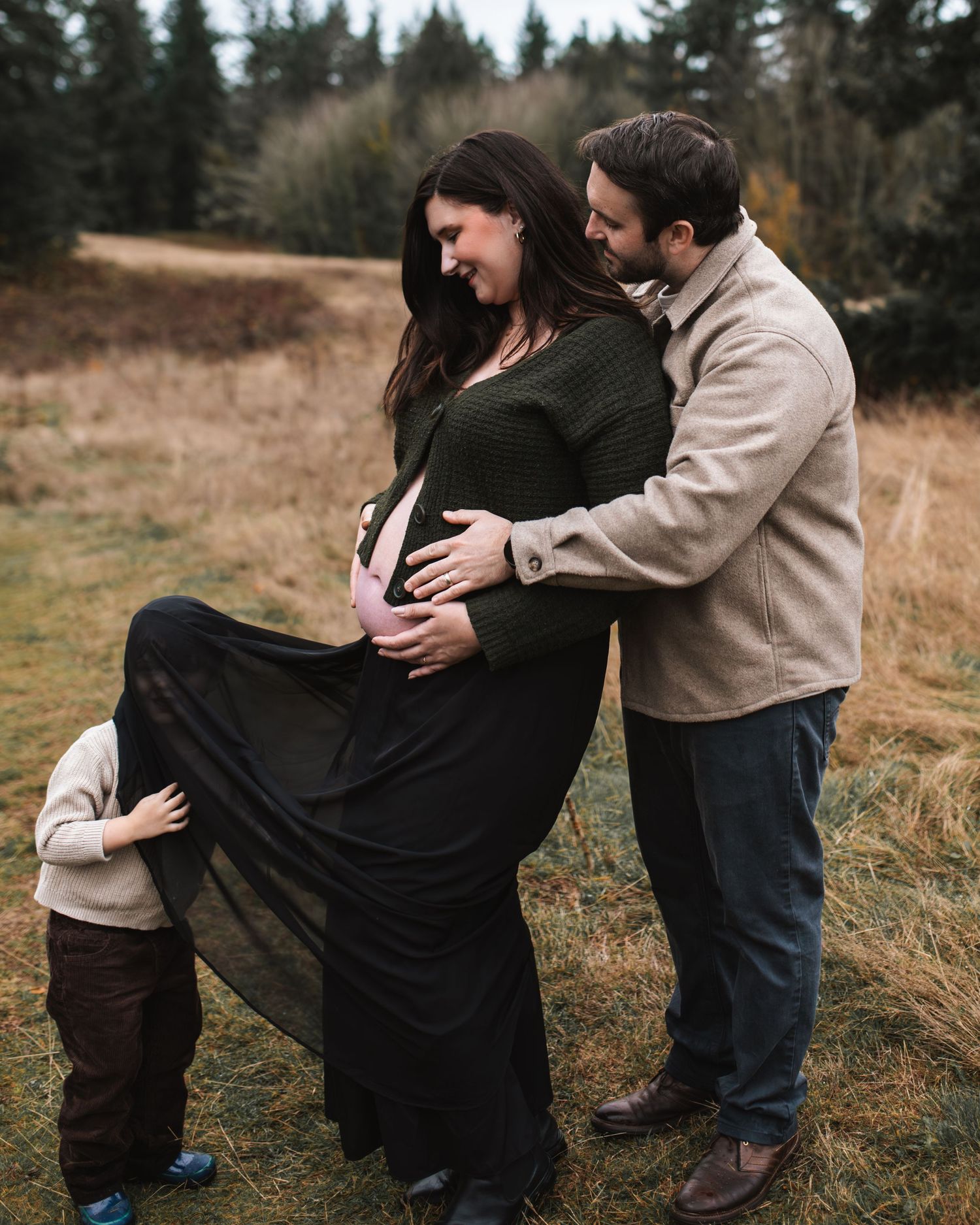 mom and dad snuggled together while son plays in moms skirt during maternity session