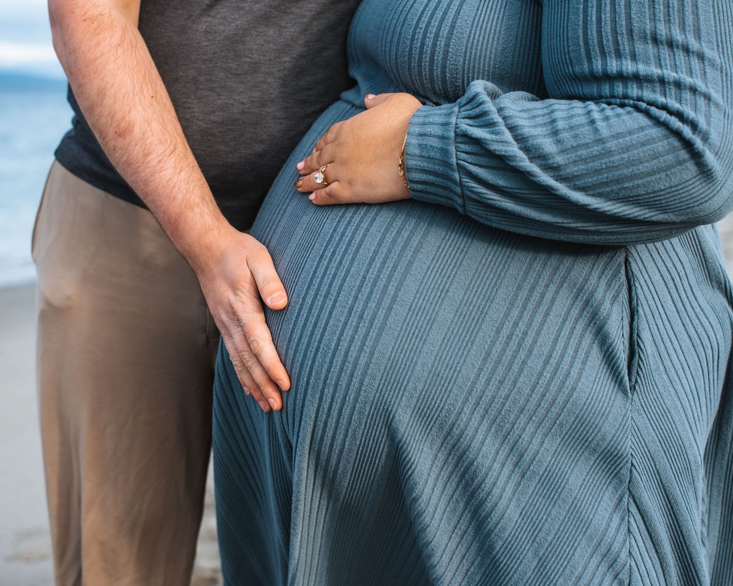 Dad rests hand on moms pregnant belly on beach during maternity session