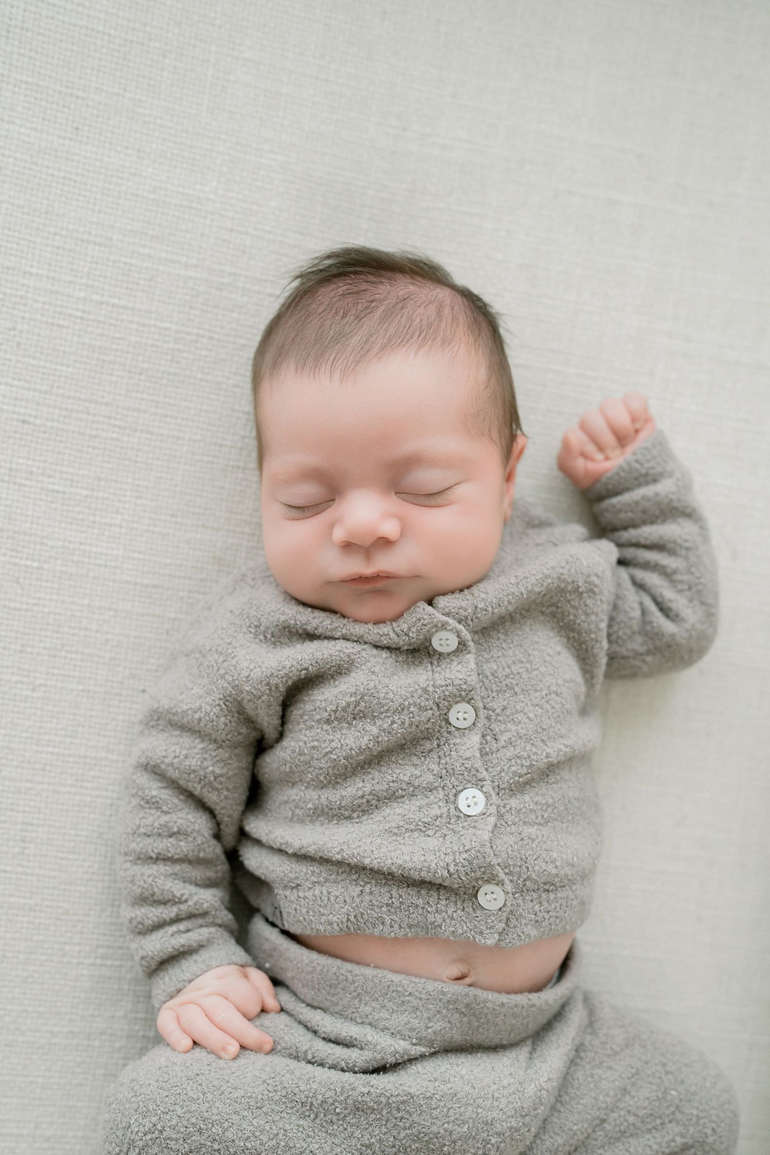 Sleeping newborn baby wearing a soft gray knit outfit, lying peacefully on a light gray blanket.