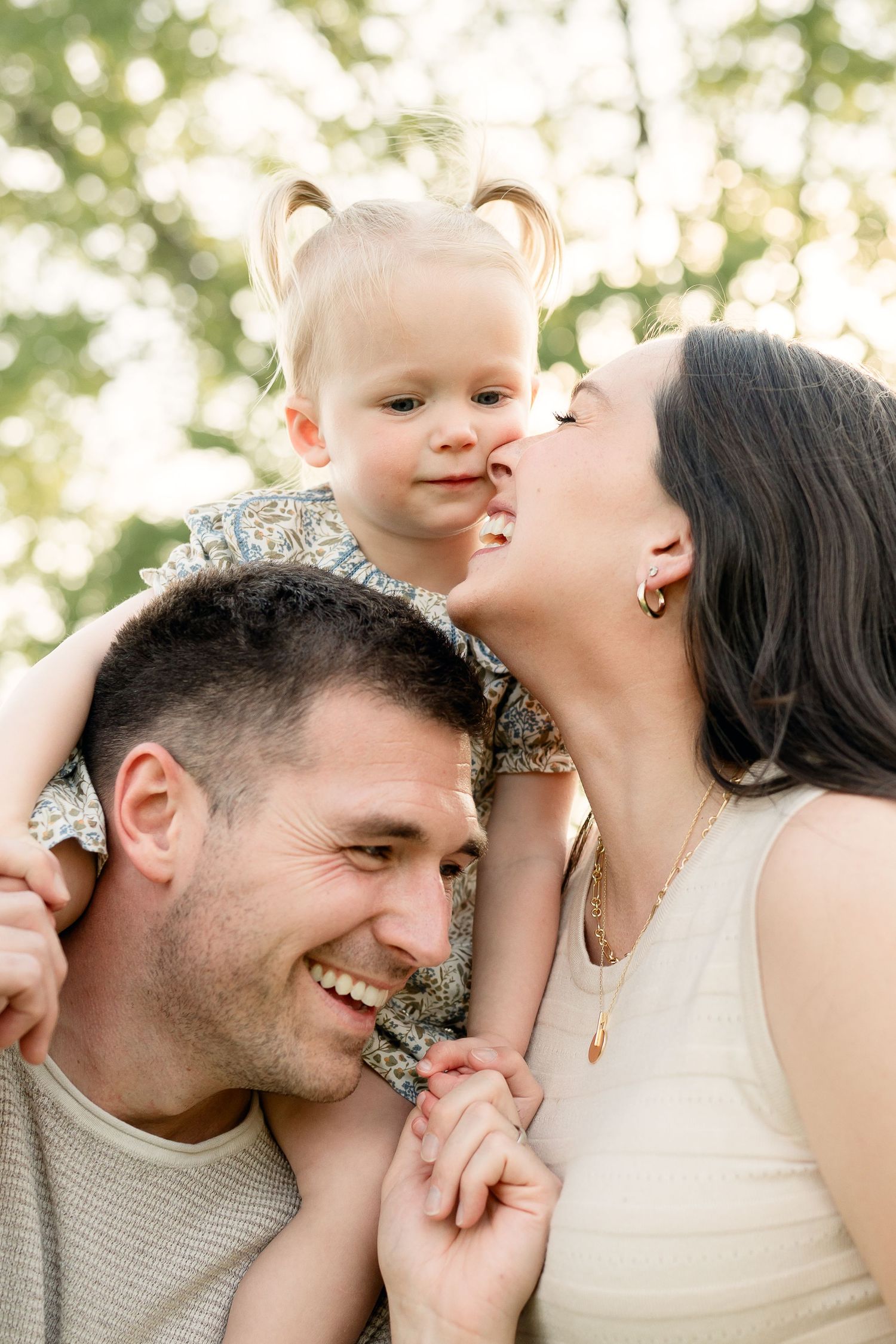 Happy family with father, mother, and toddler girl on dads shoulders outdoors.