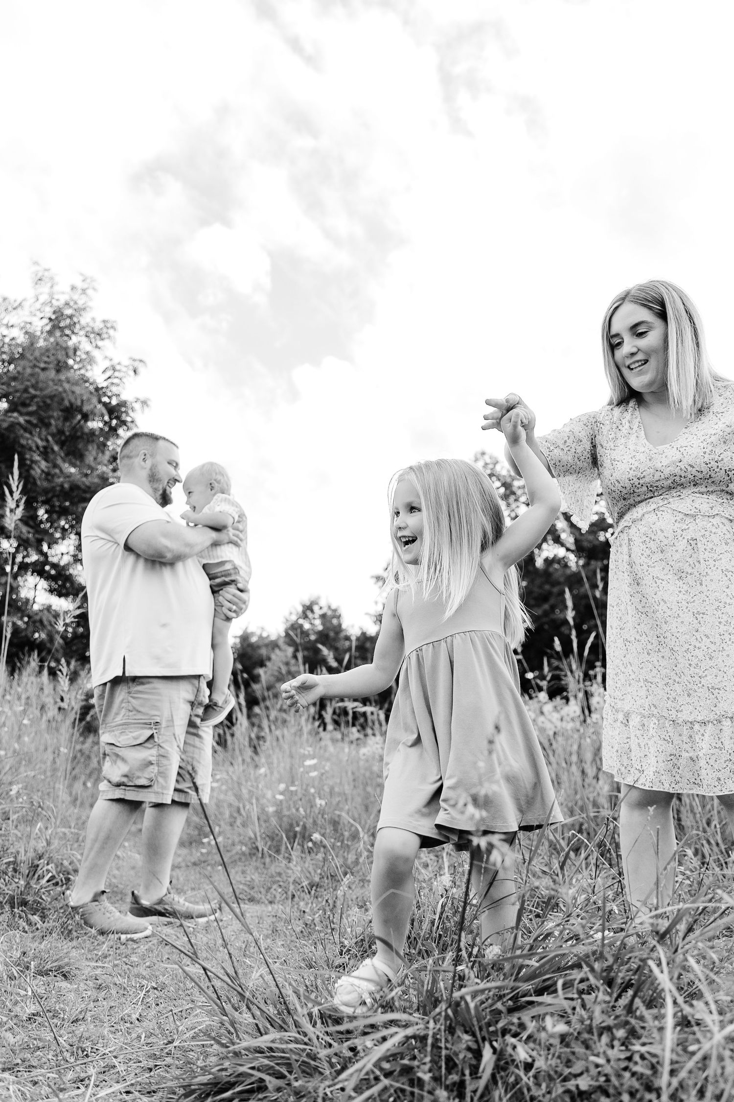 Black and white photo of family with toddler and baby playing in summer field.