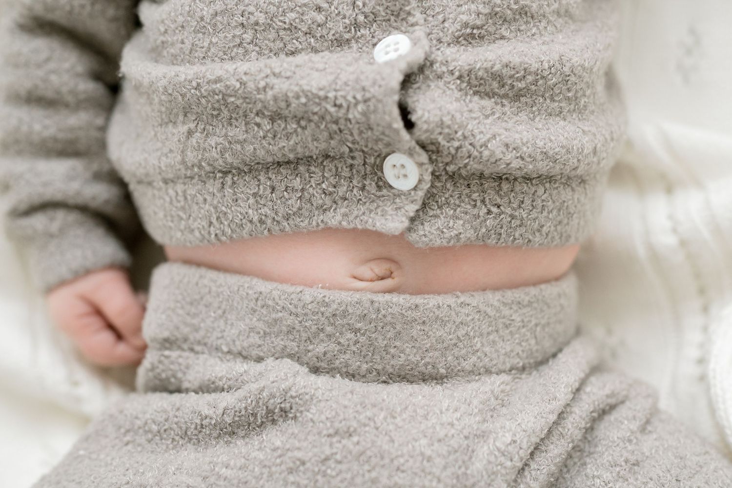 Close-up of a baby's belly button wearing a cozy gray fuzzy two-piece outfit with white buttons.