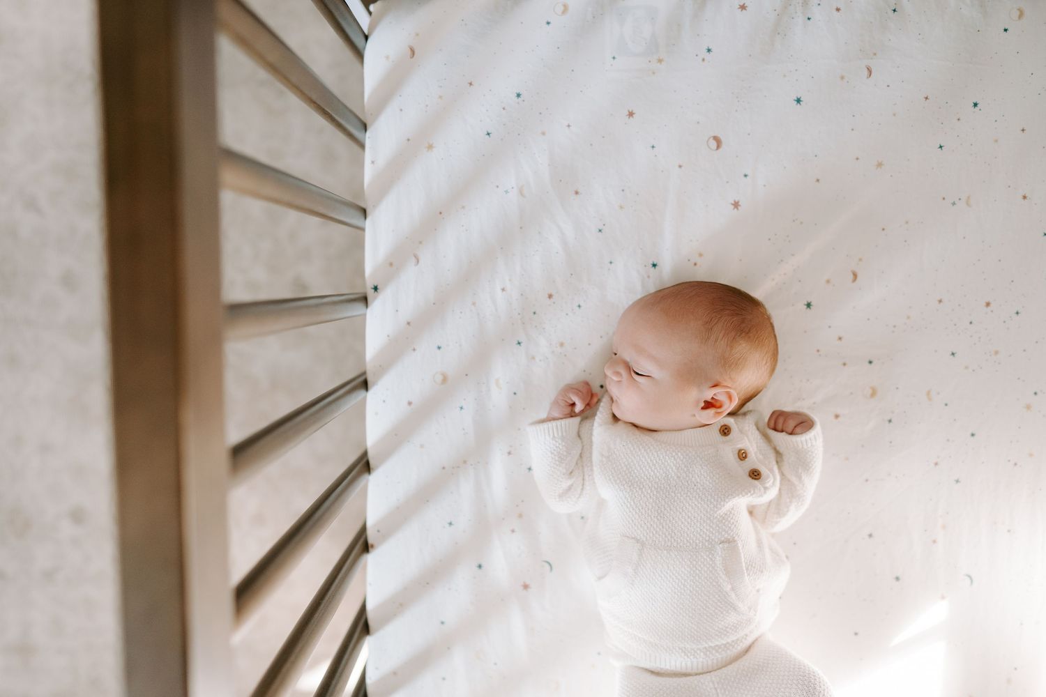 Peaceful newborn baby sleeping in a white crib wearing a soft white onesie.