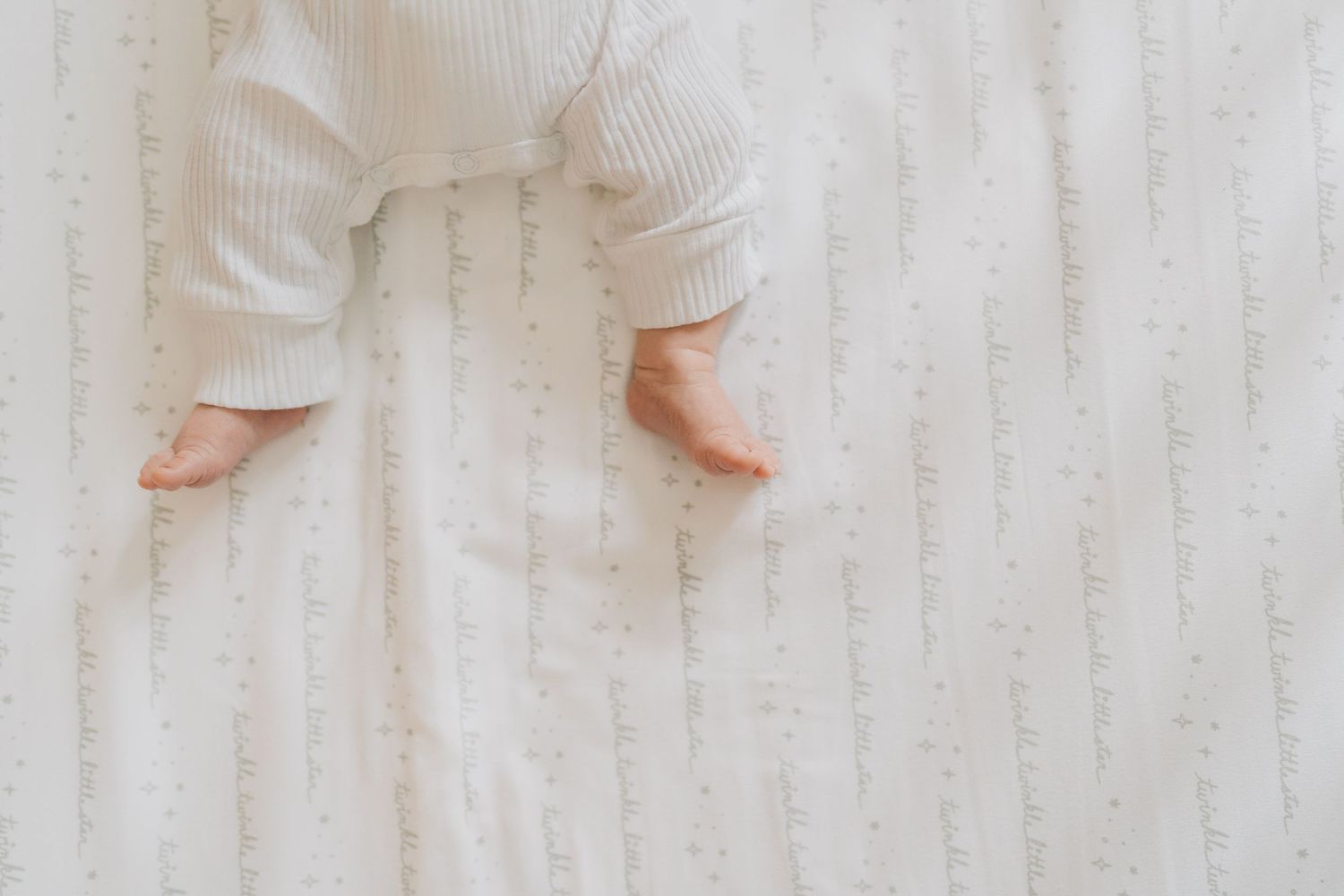 Close-up of a newborn baby's tiny bare feet lying on a soft white textured blanket.