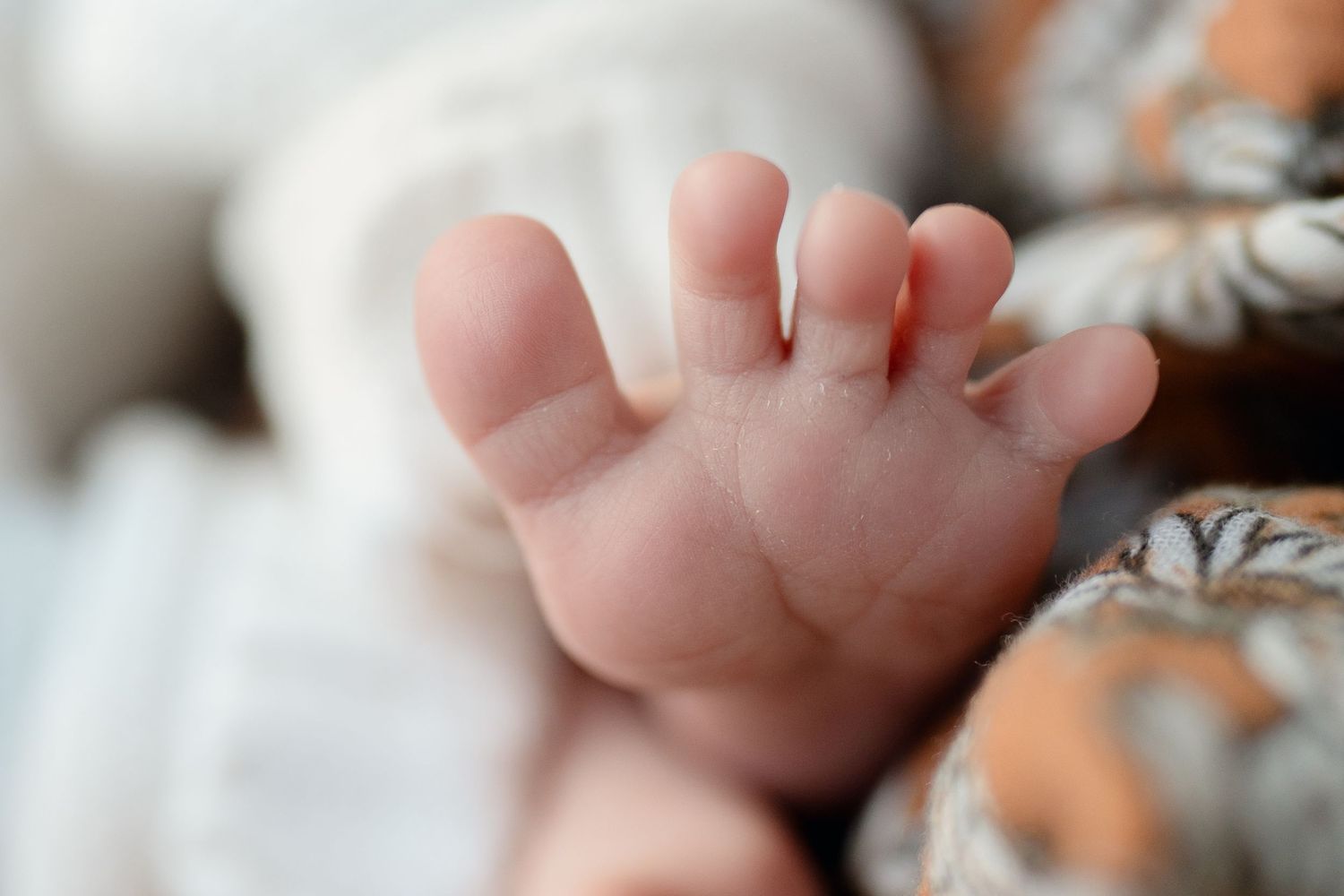 Close-up of a newborn baby's tiny foot and toes, with soft blurred background.
