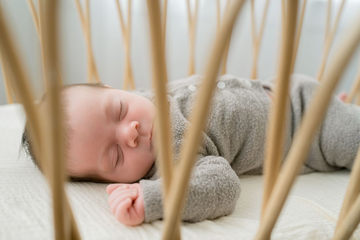 Peaceful newborn baby sleeping soundly in a modern wooden crib, dressed in a soft gray onesie.