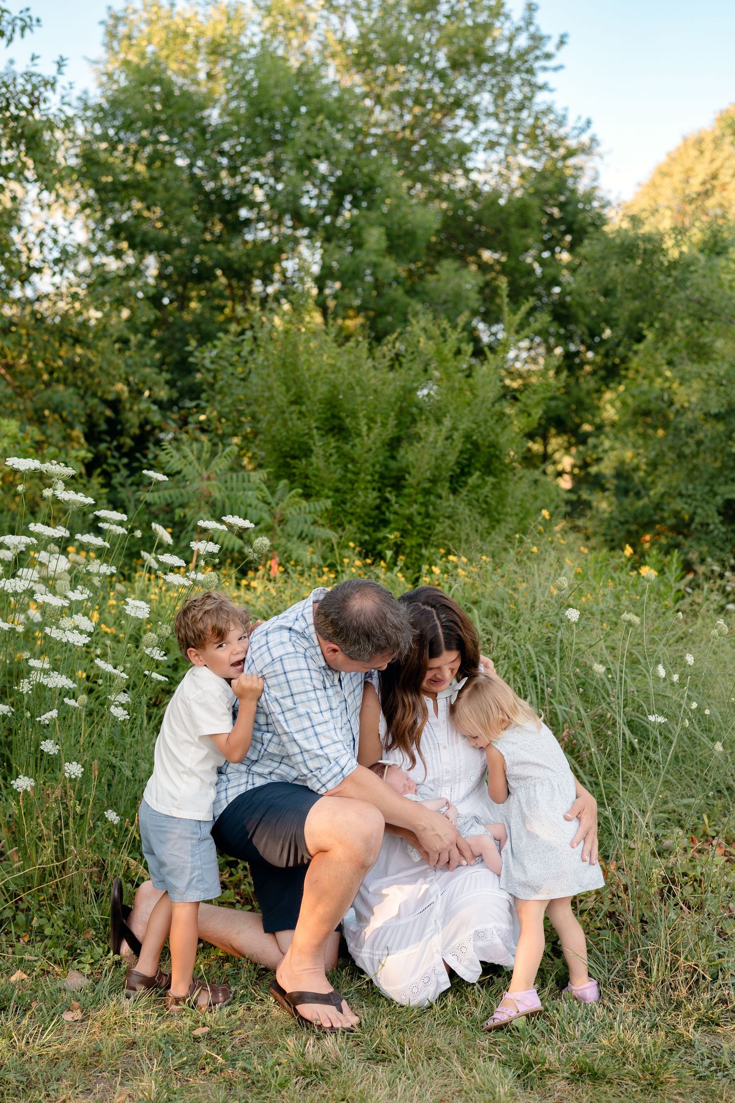 Happy family with two young children sharing a joyful embrace in a lush green meadow with wildflowers.