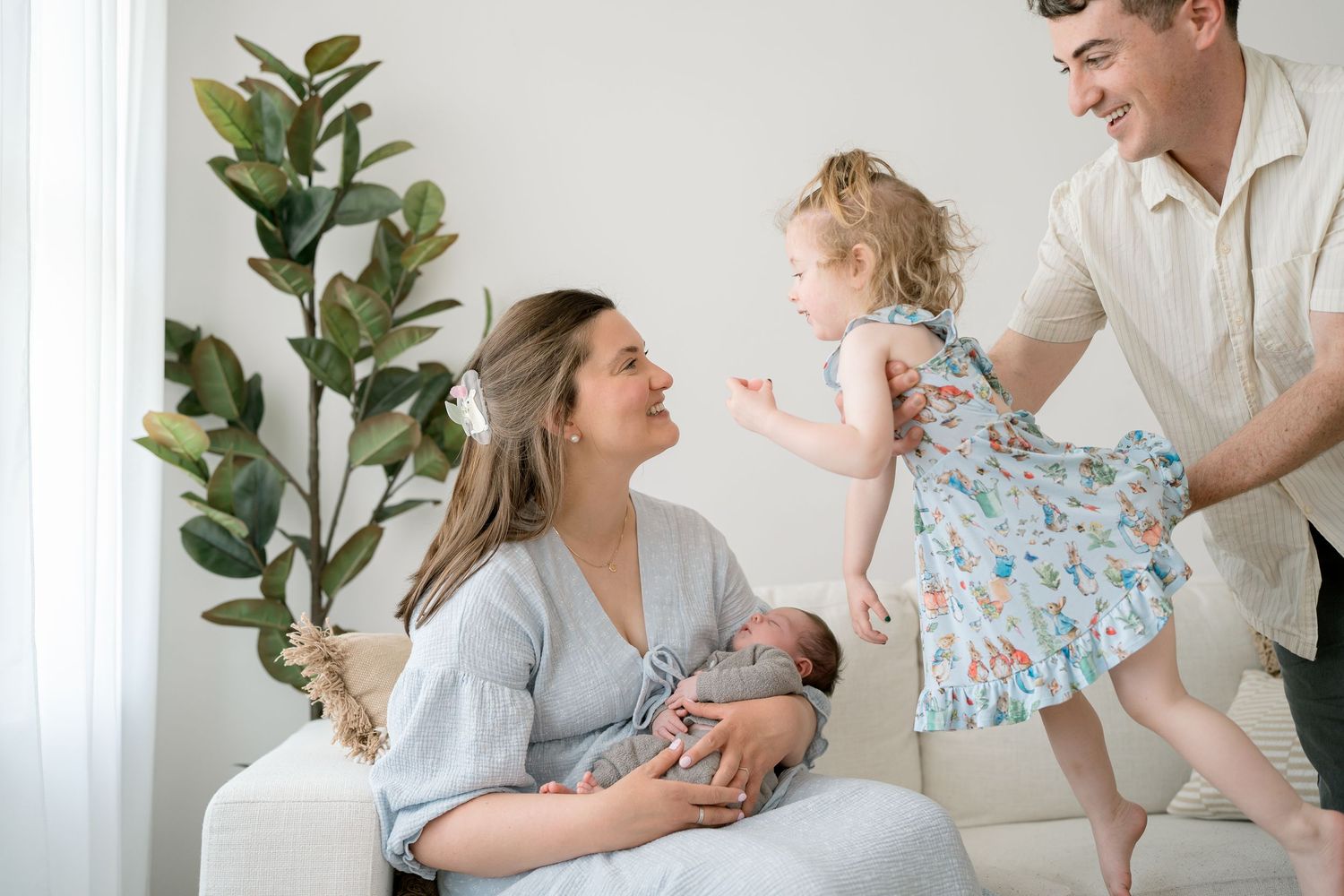 Happy family with newborn baby and toddler girl in bright white living room during professional photo session.
