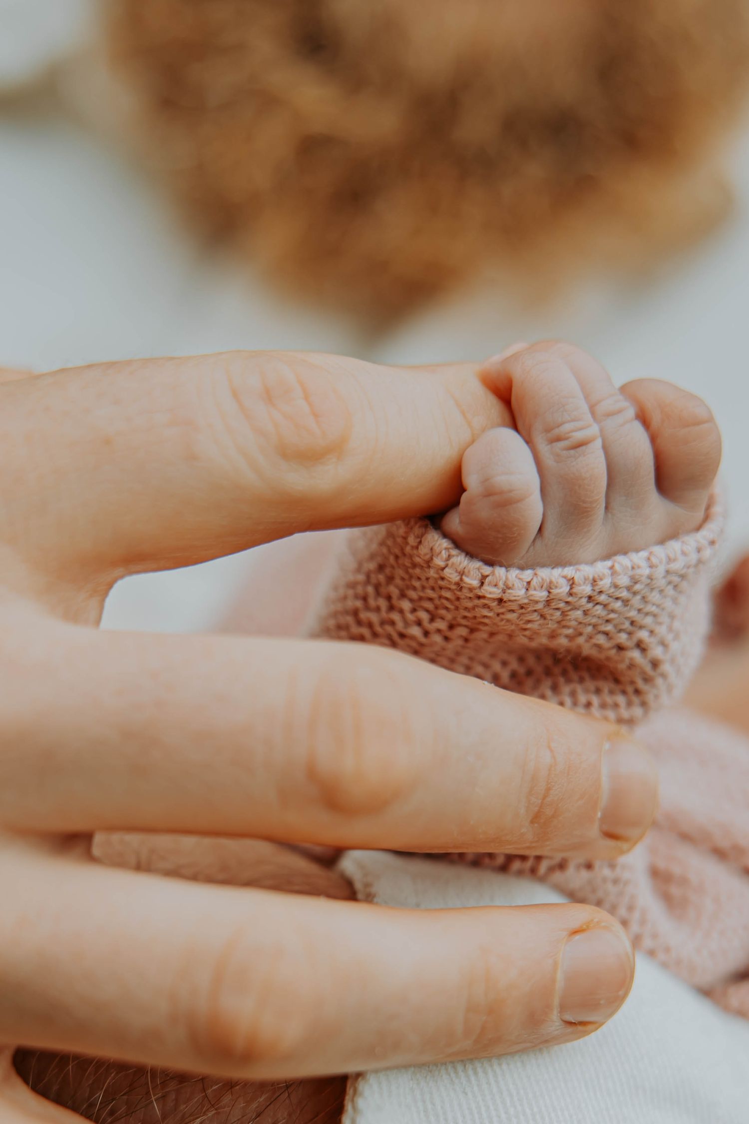 Gentle hands massaging a small foot wrapped in knitted brown fabric.