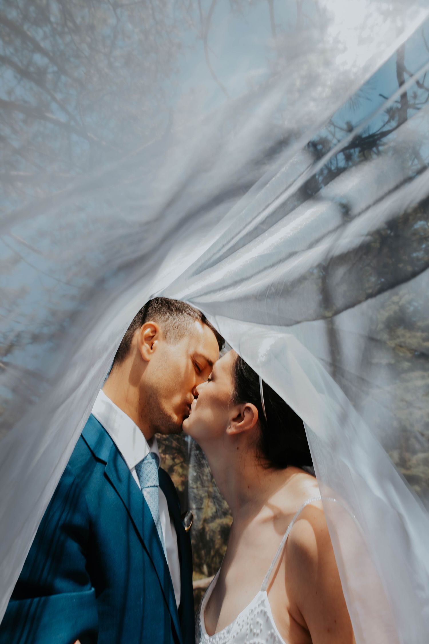 An intimate wedding moment captured under flowing white veil with dramatic lighting.