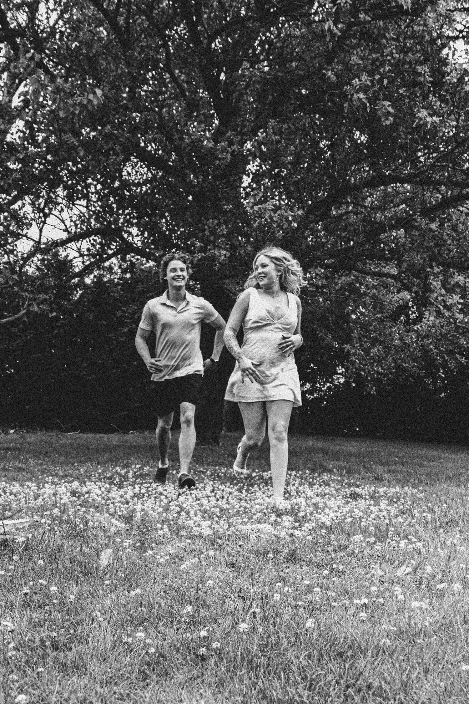 A joyful couple running together through a meadow with blooming wildflowers, captured in black and white.