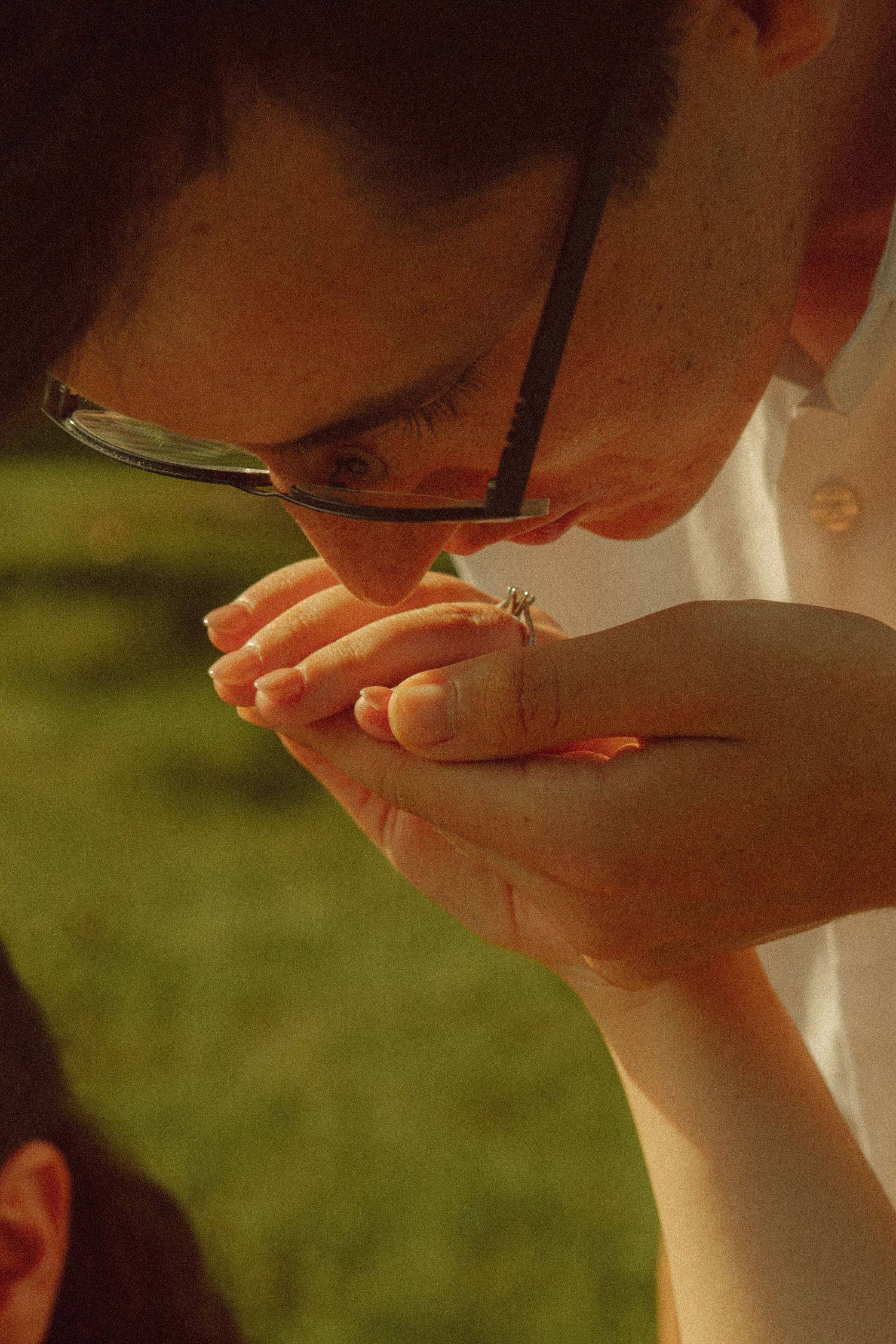 Person with glasses closely examining a small insect resting on cupped hands outdoors.