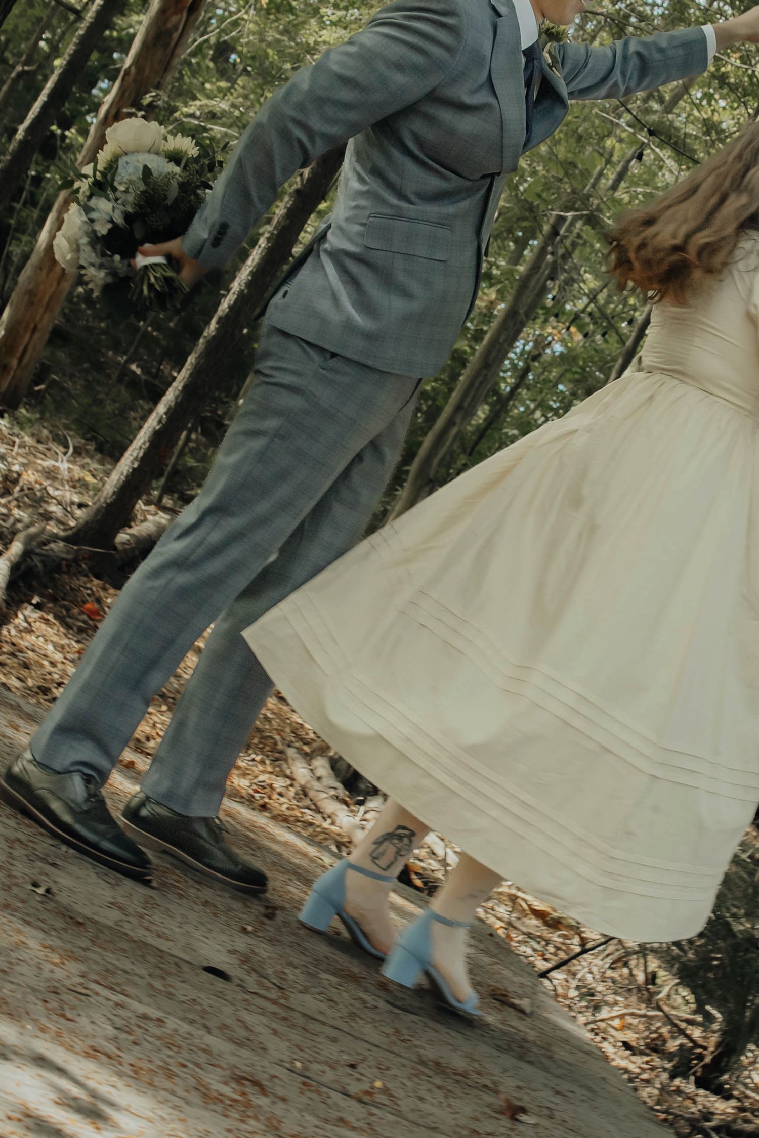 A couple dances together in an outdoor setting, the bride in white and groom in grey.
