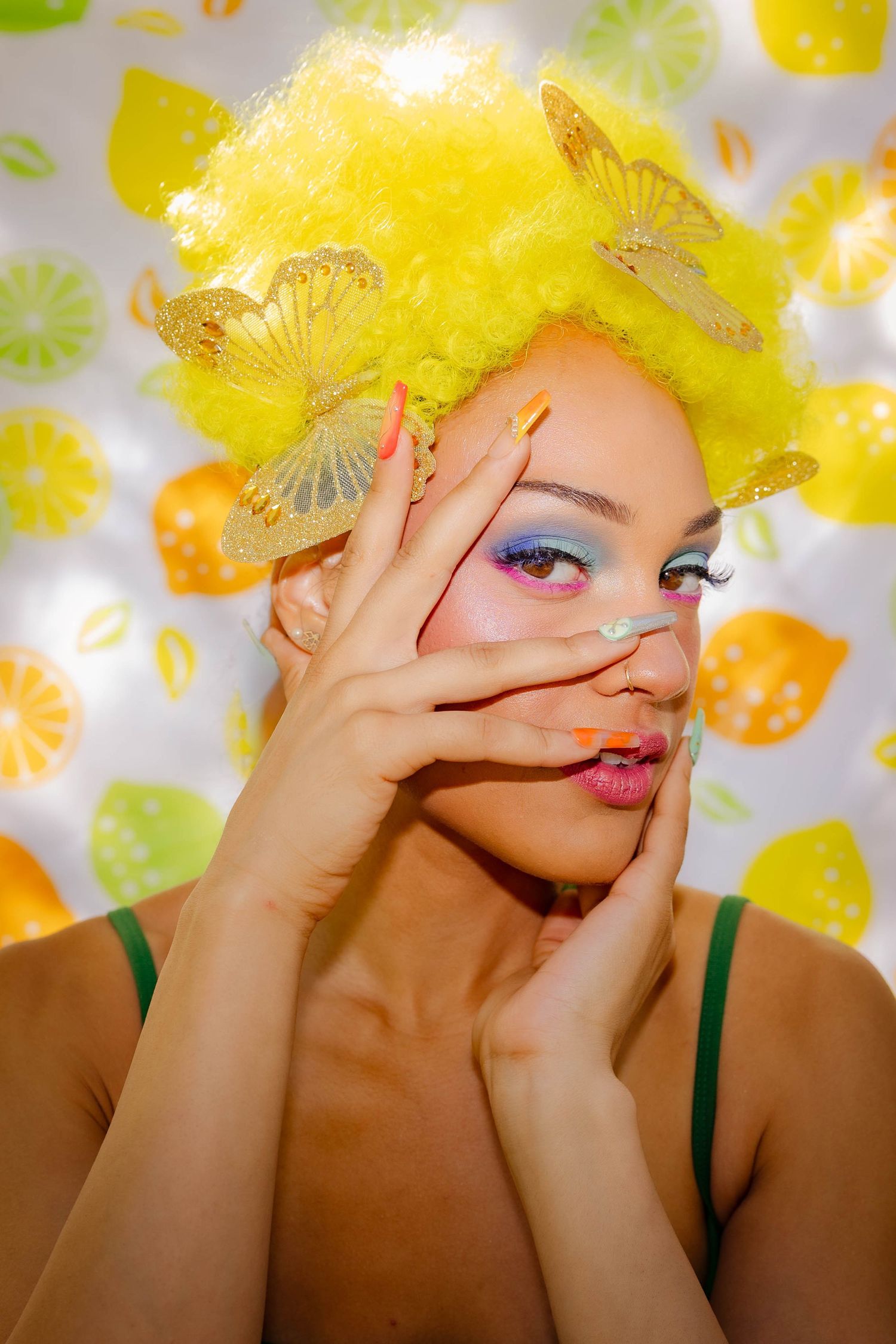A series of four photos showing colorful makeup and yellow hair against a citrus-patterned background.