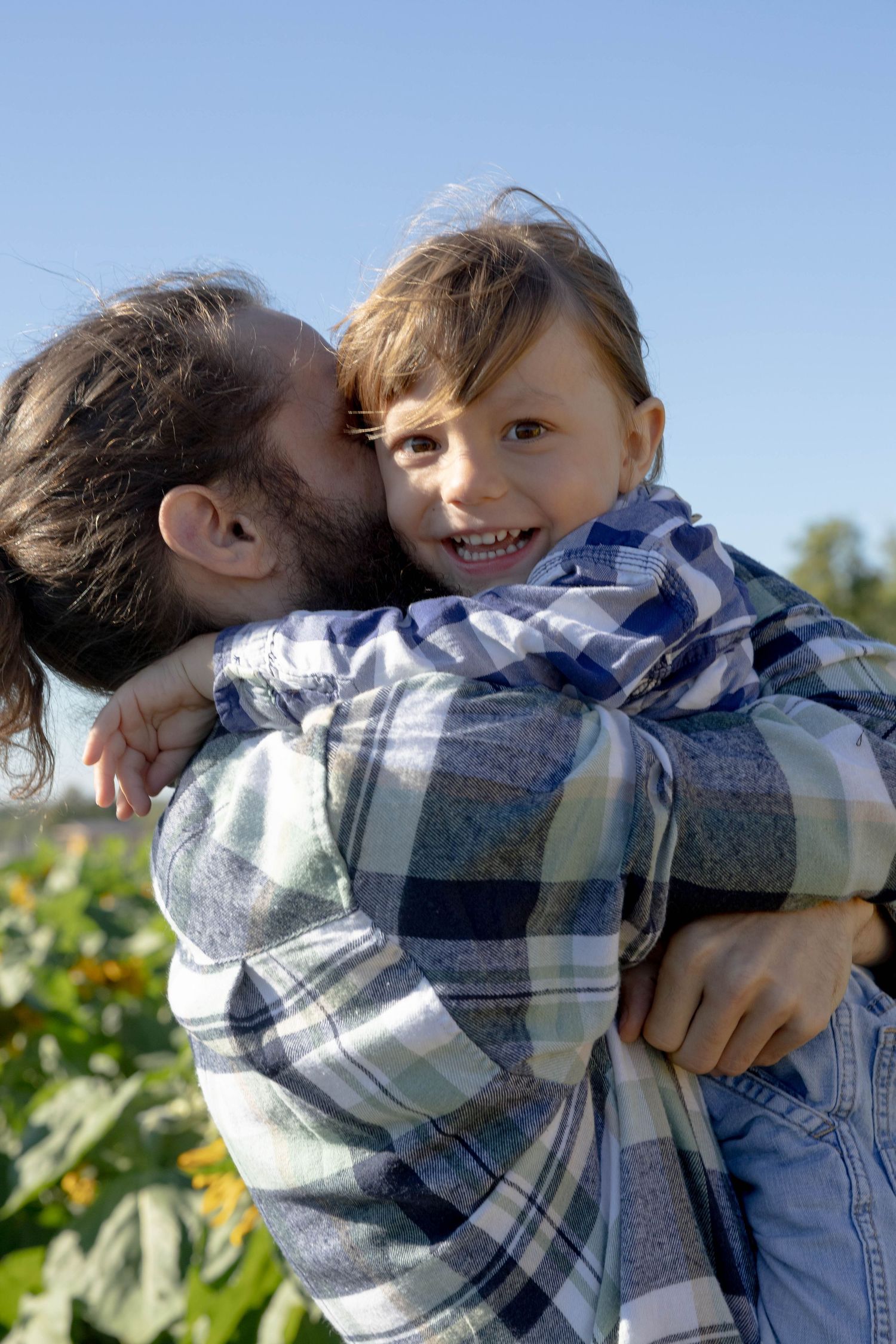 A playful moment captured in plaid shirts against a bright blue sky and green foliage background.