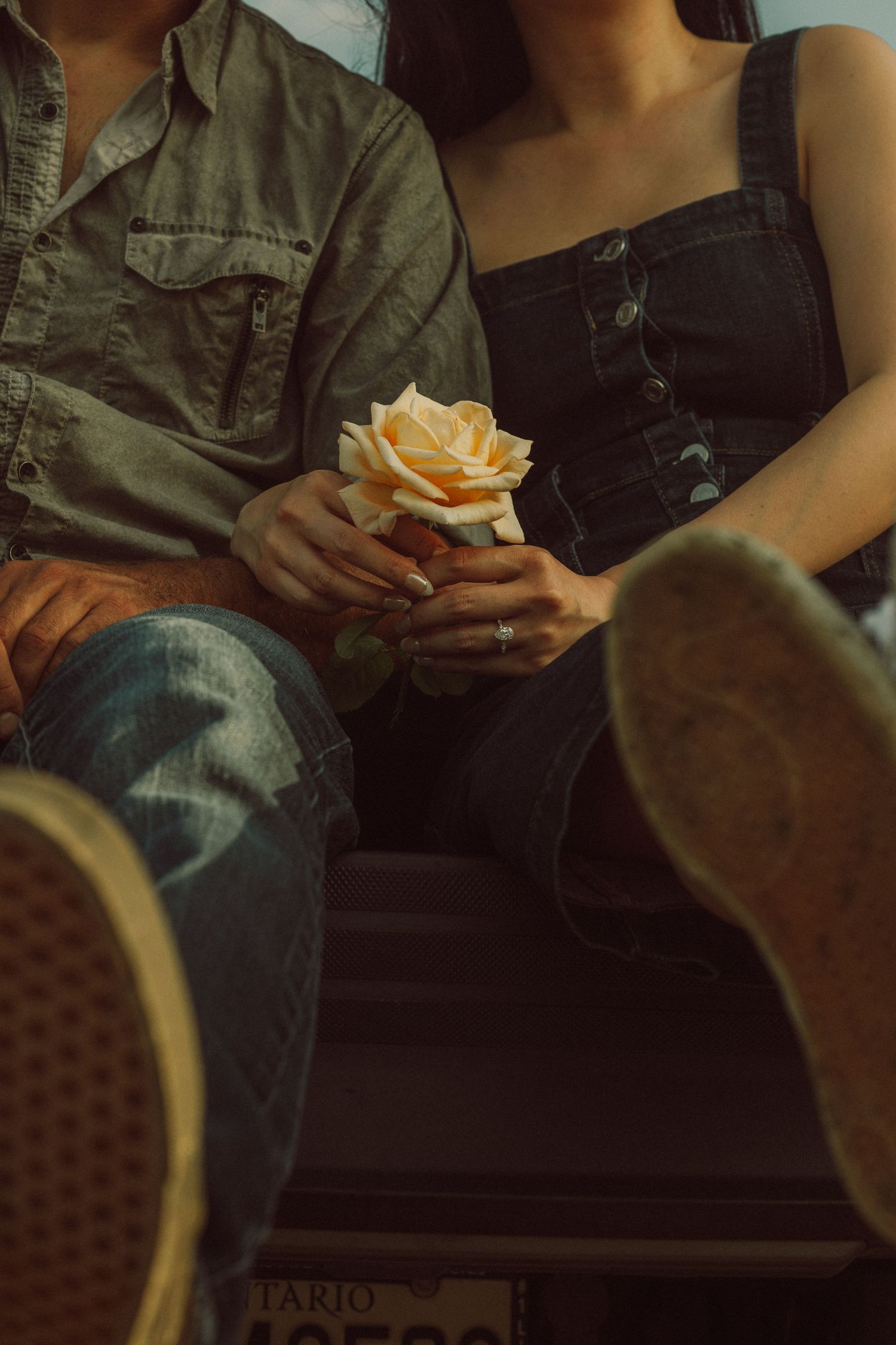 Couple sitting together holding a peach rose, wearing denim outfits, with sneakers visible in the foreground.