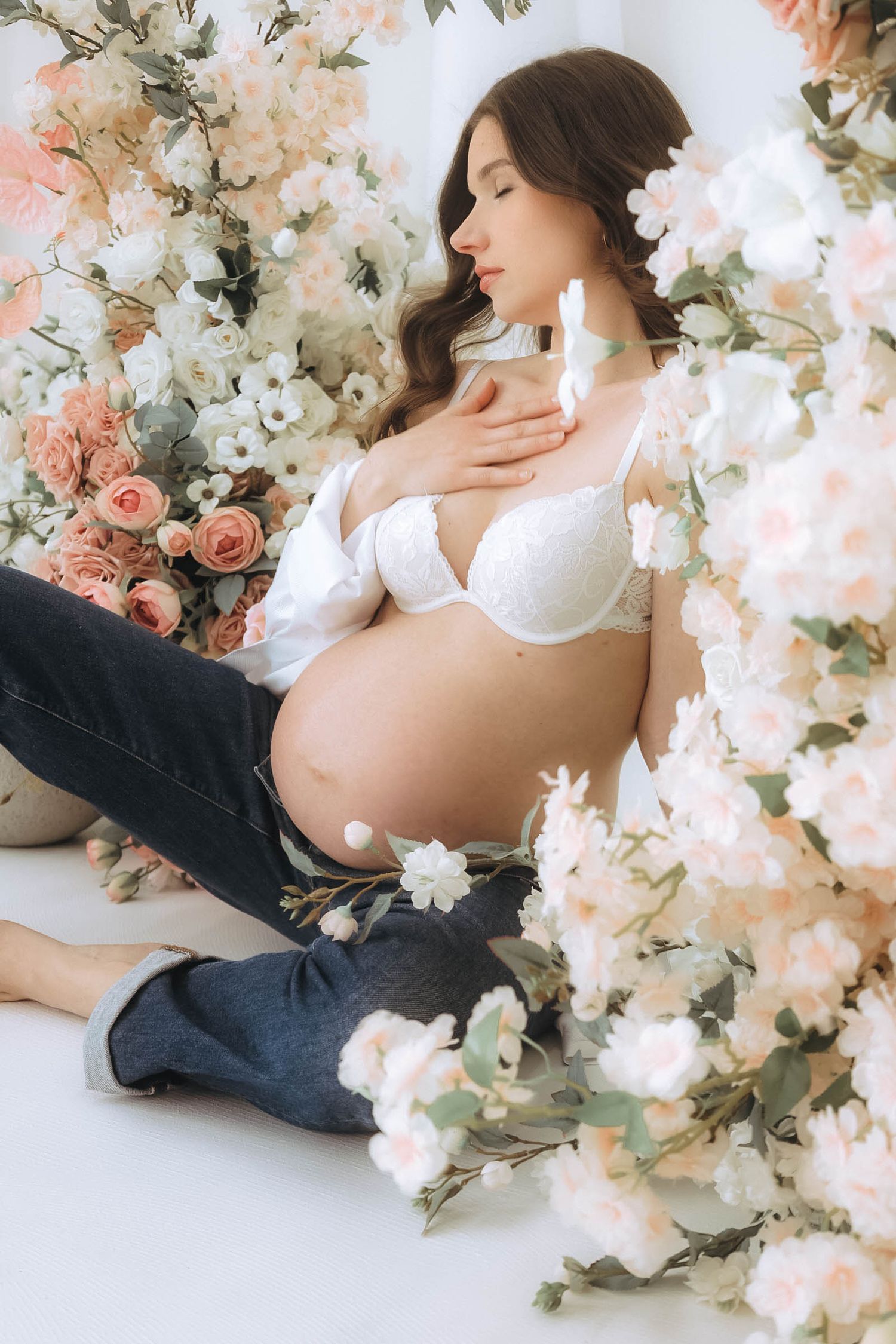 An artistic maternity portrait surrounded by soft pink and white floral arrangements.
