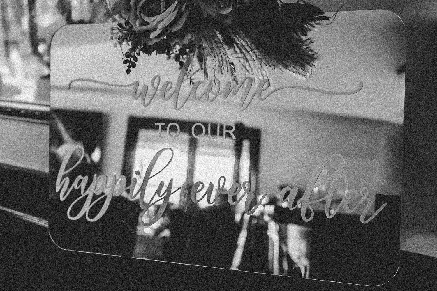 A black and white photograph shows a blurry welcome sign with cursive text on display.