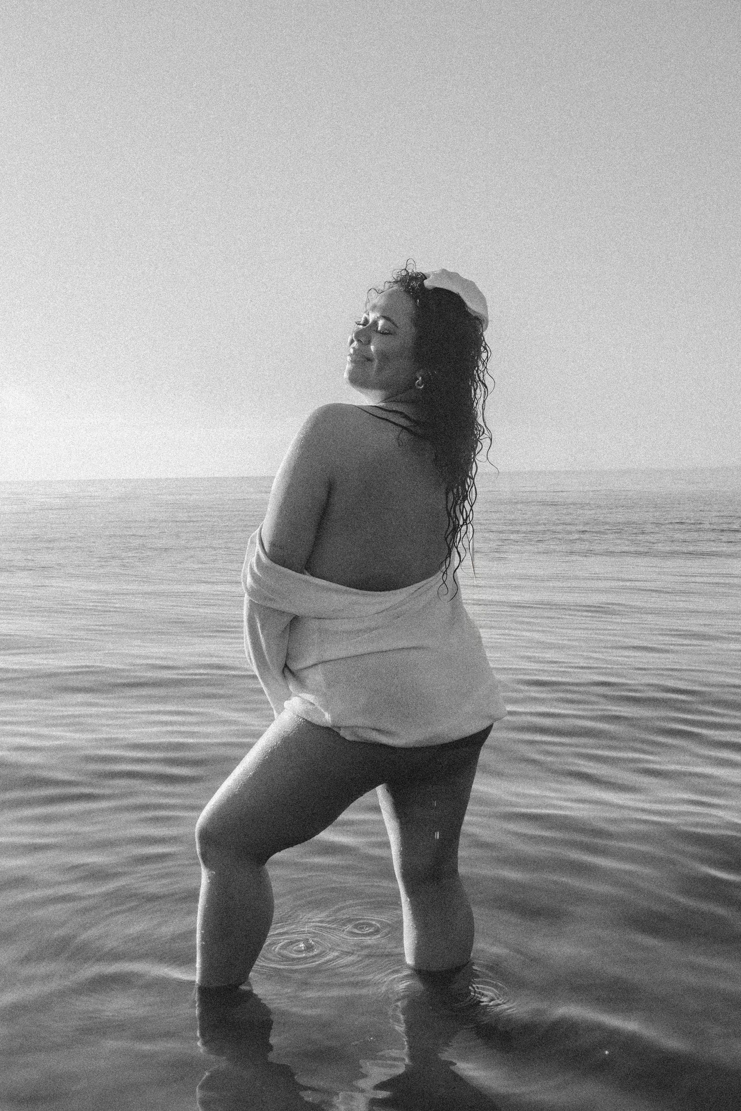 A black and white photo of someone standing in ocean water wearing a light-colored dress.