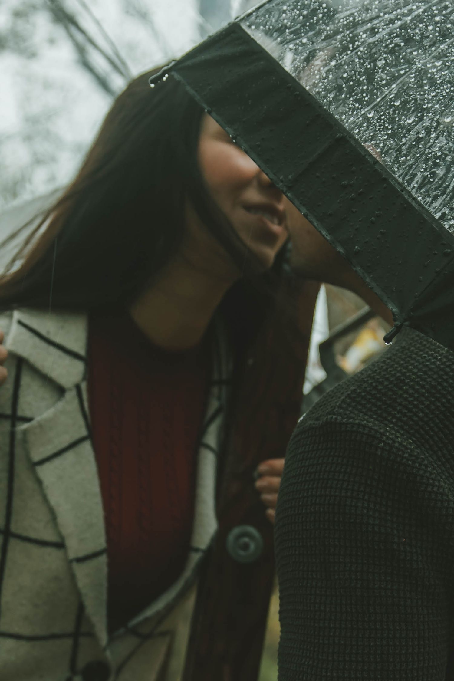 Two people share a close moment beneath a transparent umbrella on a rainy day.