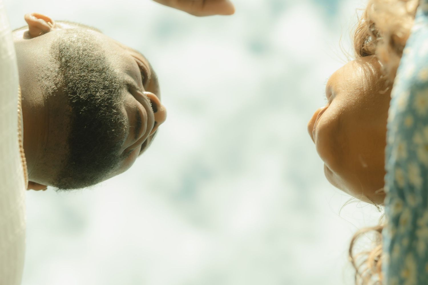 Close-up low-angle view of couple facing each other intimately against bright sky background.