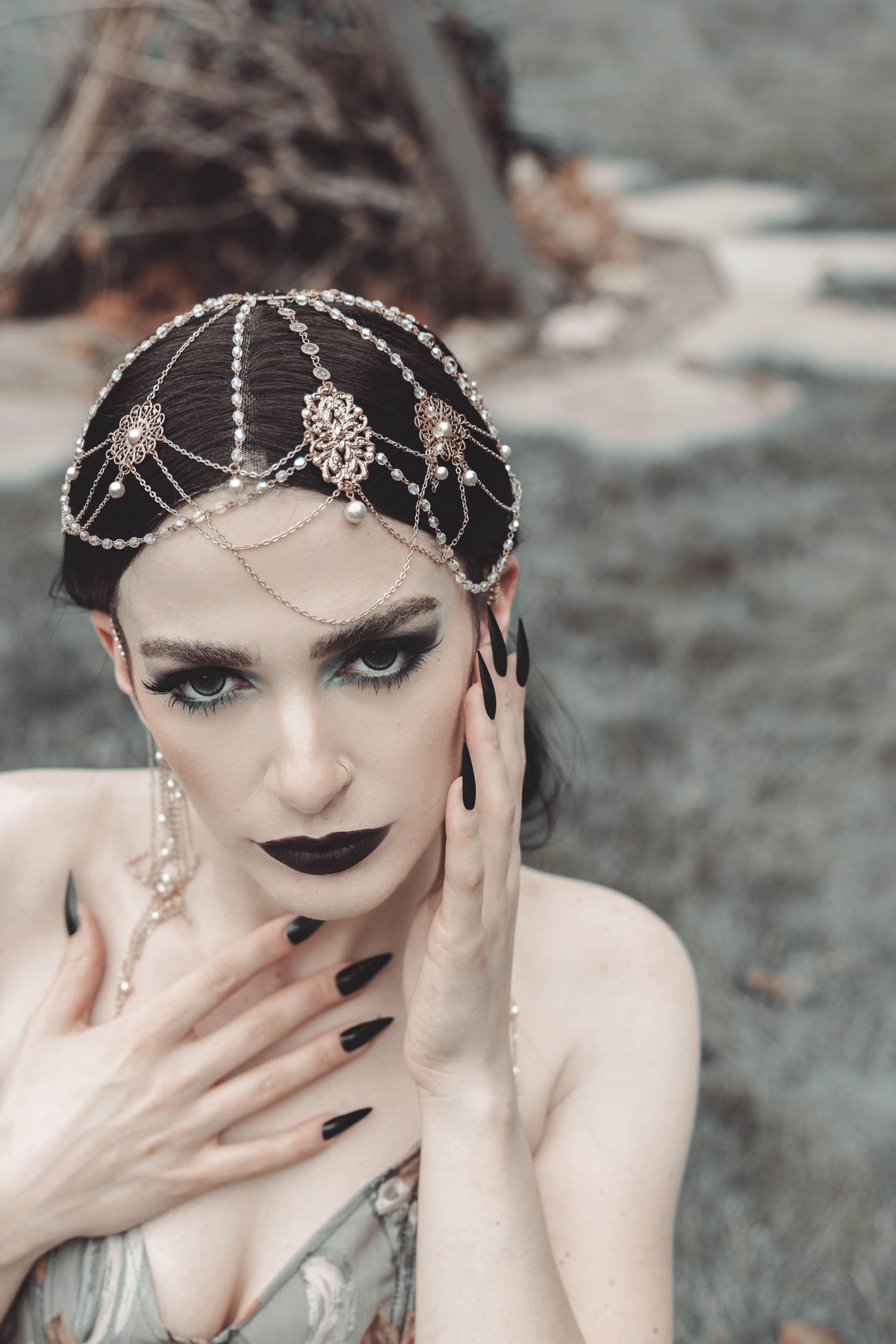 Gothic glamour portrait with crystal headpiece and dramatic black nail polish against muted background.