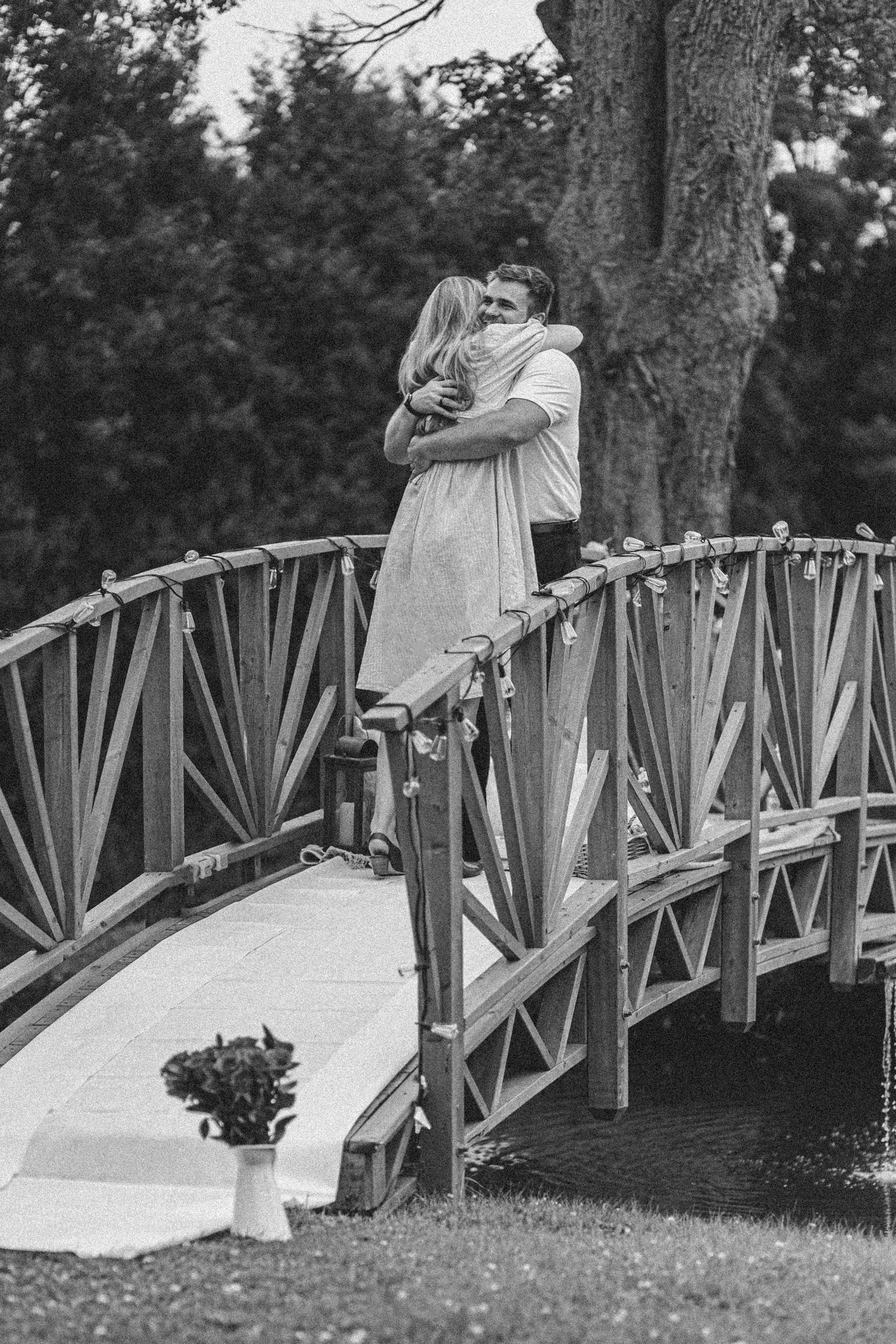 A romantic couple in wedding attire shares tender moments on a wooden footbridge in a peaceful garden setting.