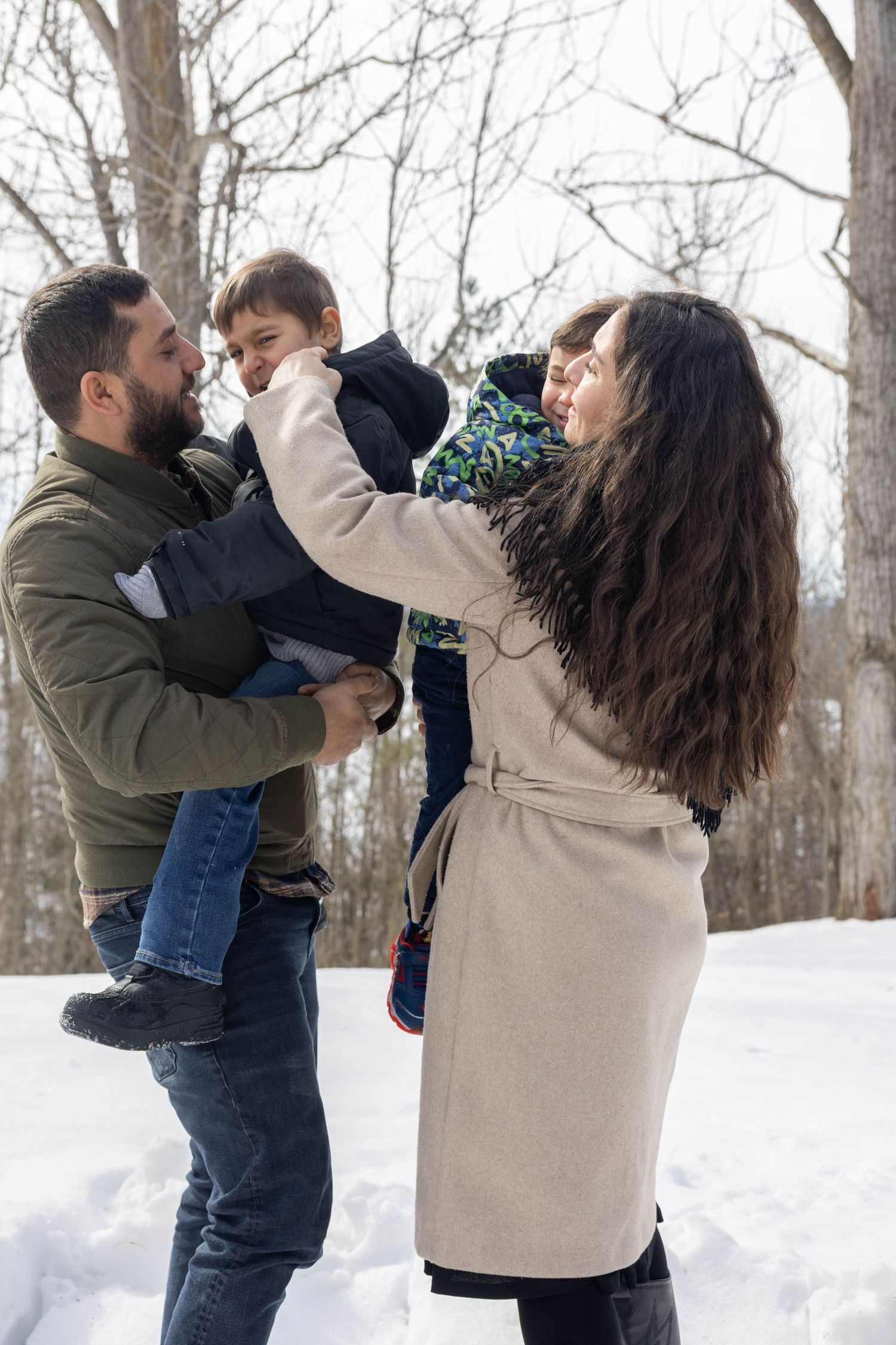 A family plays together outdoors in the snow on a winter day, wearing warm coats and sharing joyful moments.