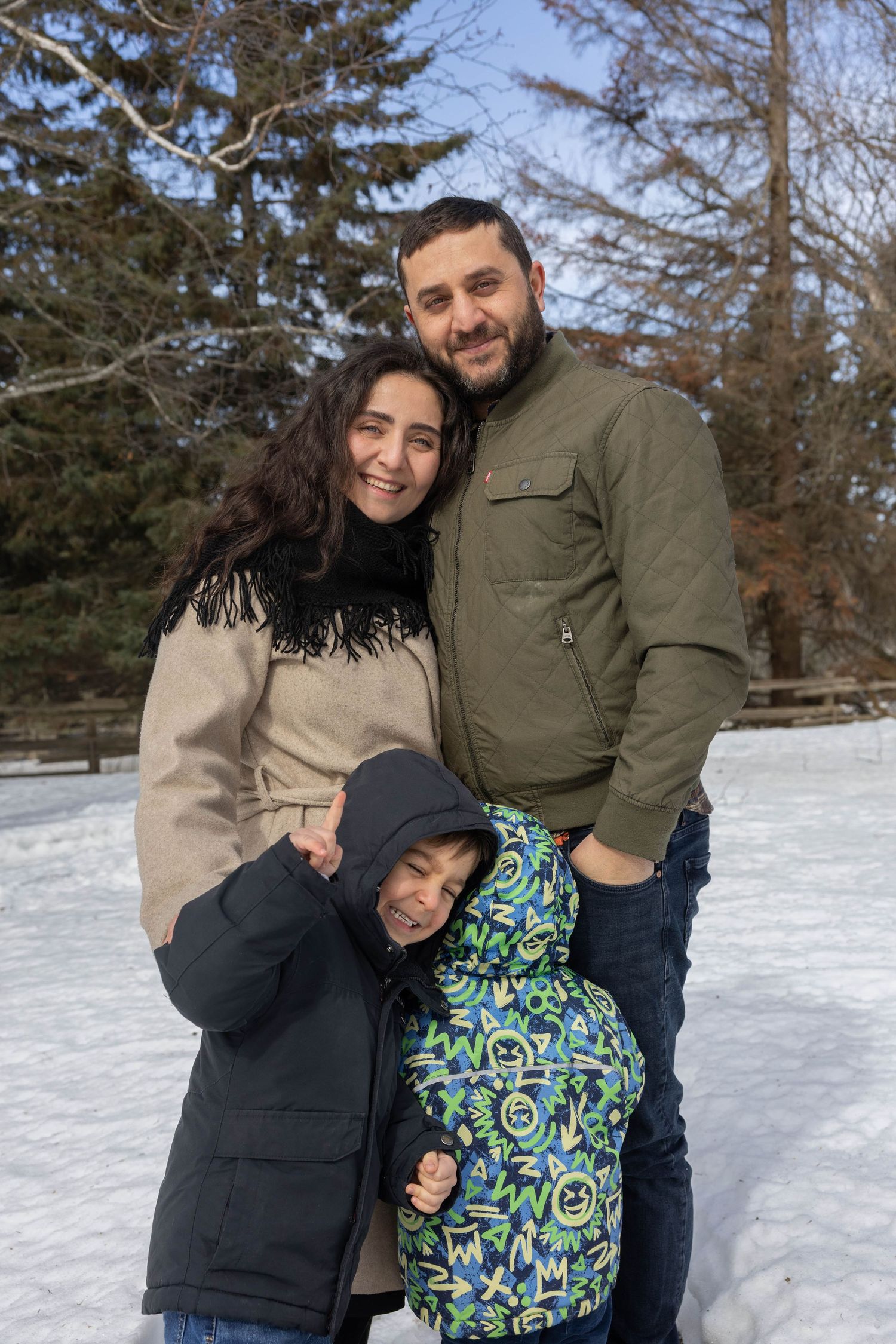 A family enjoys a winter day together in the snow, wearing warm coats and sharing embraces in a snowy outdoor setting.