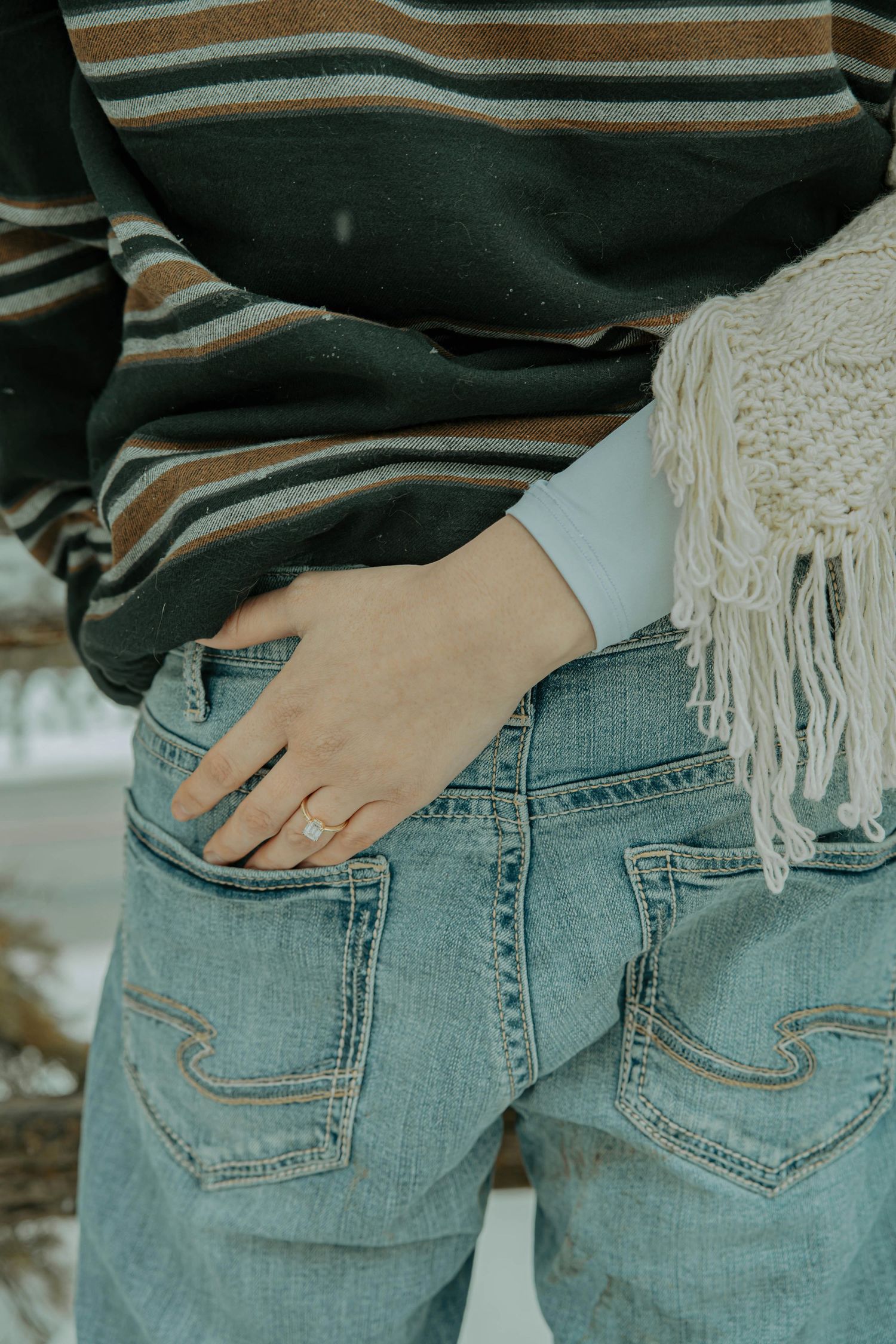 Close-up view of hands in back pockets of light wash denim jeans with decorative stitching detail.