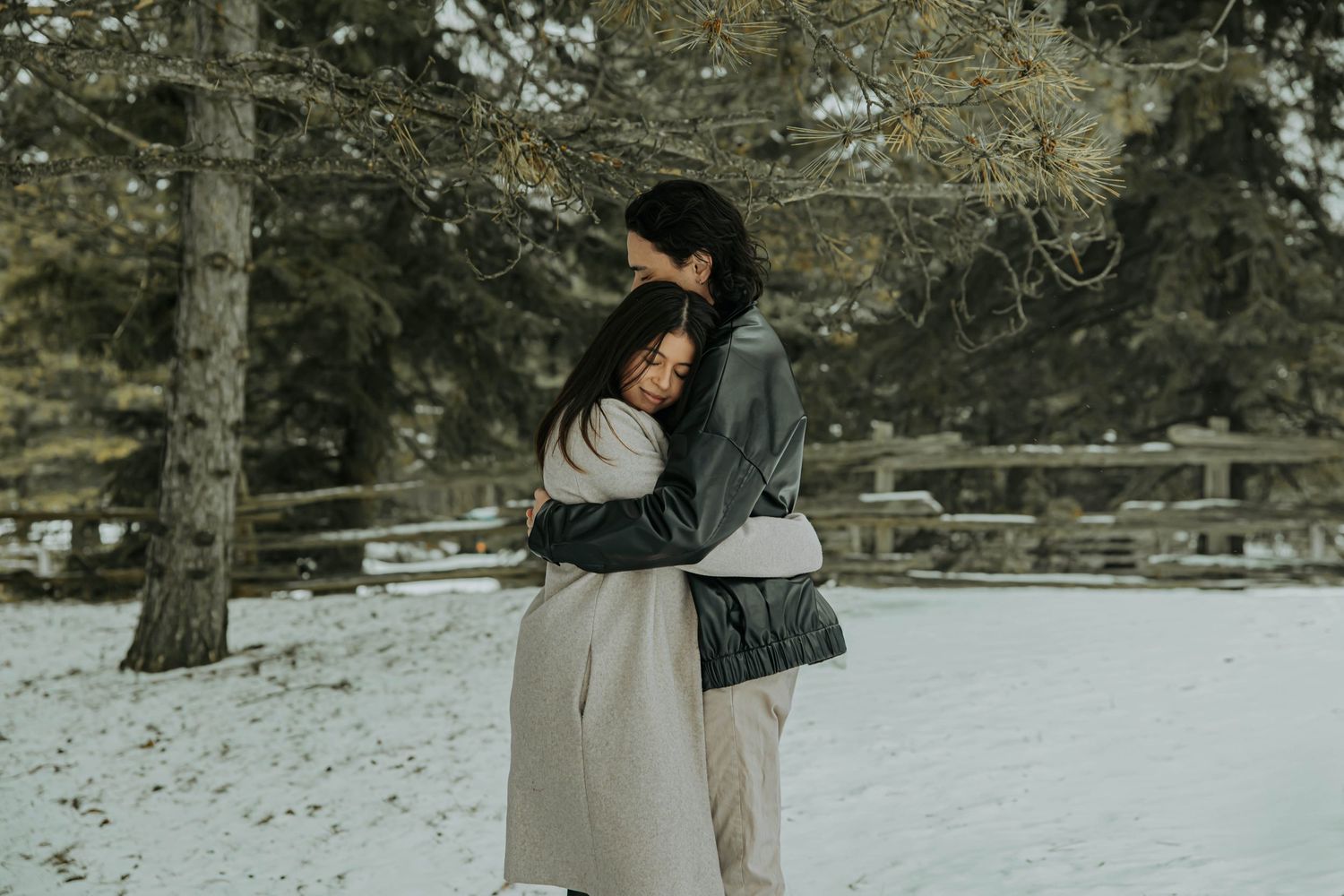 A couple embraces in a snowy winter forest setting during a romantic outdoor photoshoot.