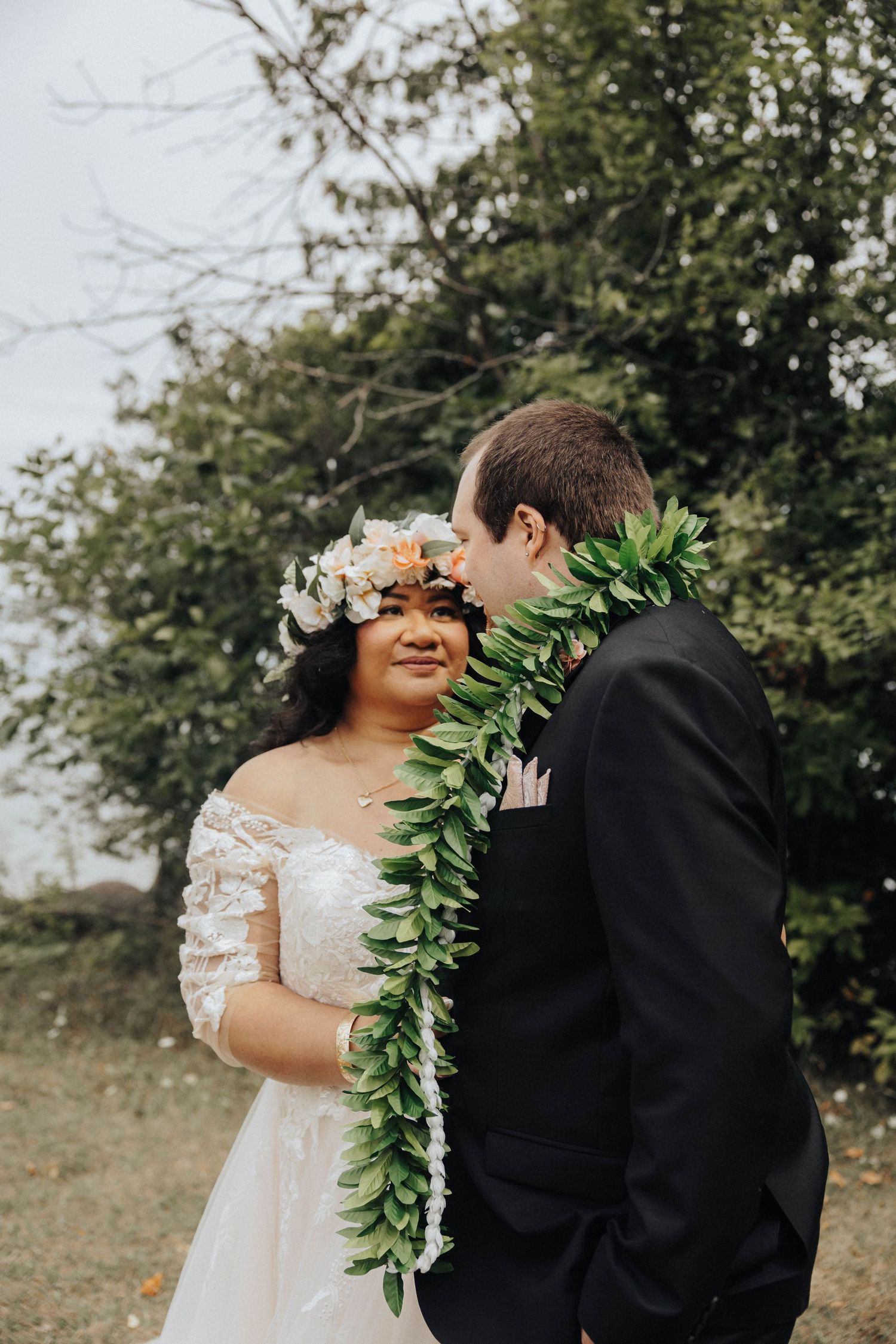Couple wearing wedding attire standing together with greenery and floral decorations in an outdoor setting.