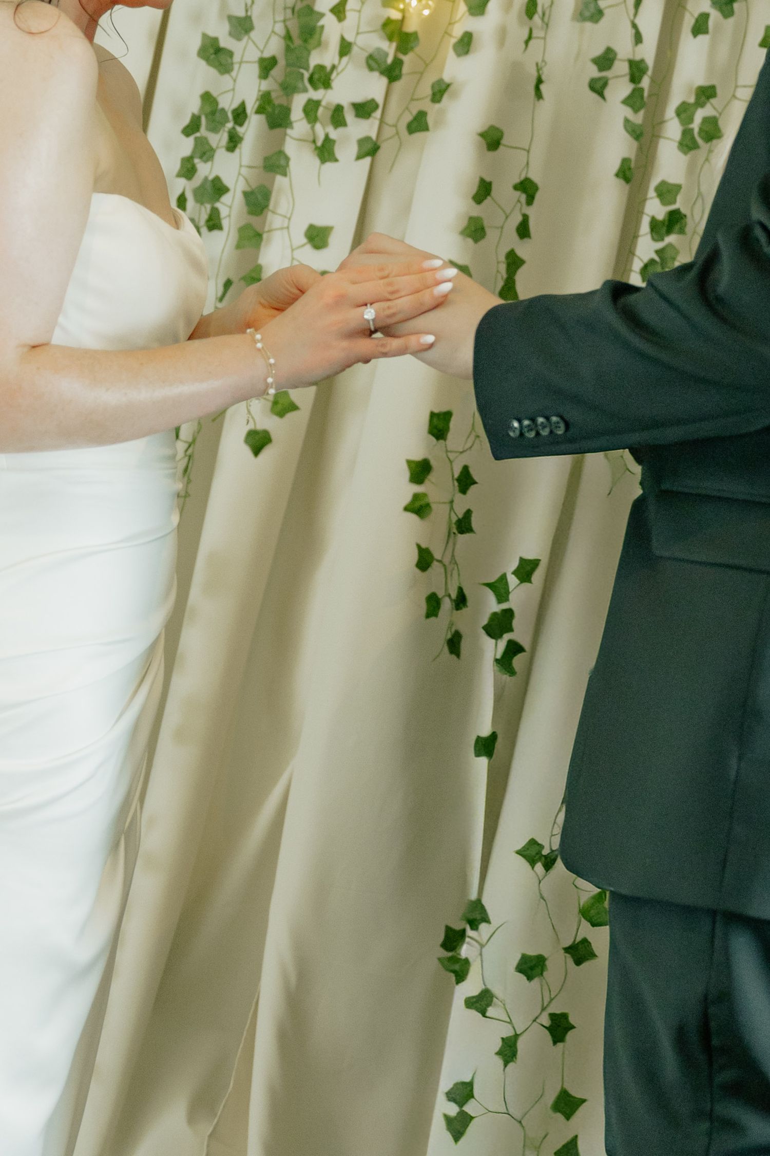 Bride and groom exchanging rings at wedding ceremony with ivy backdrop.