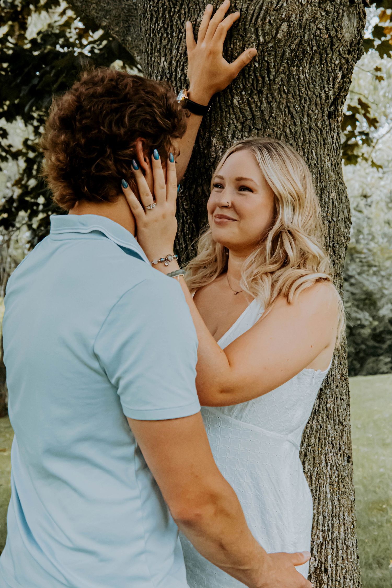 Romantic couples photoshoot sequence against large tree trunk in soft lighting.