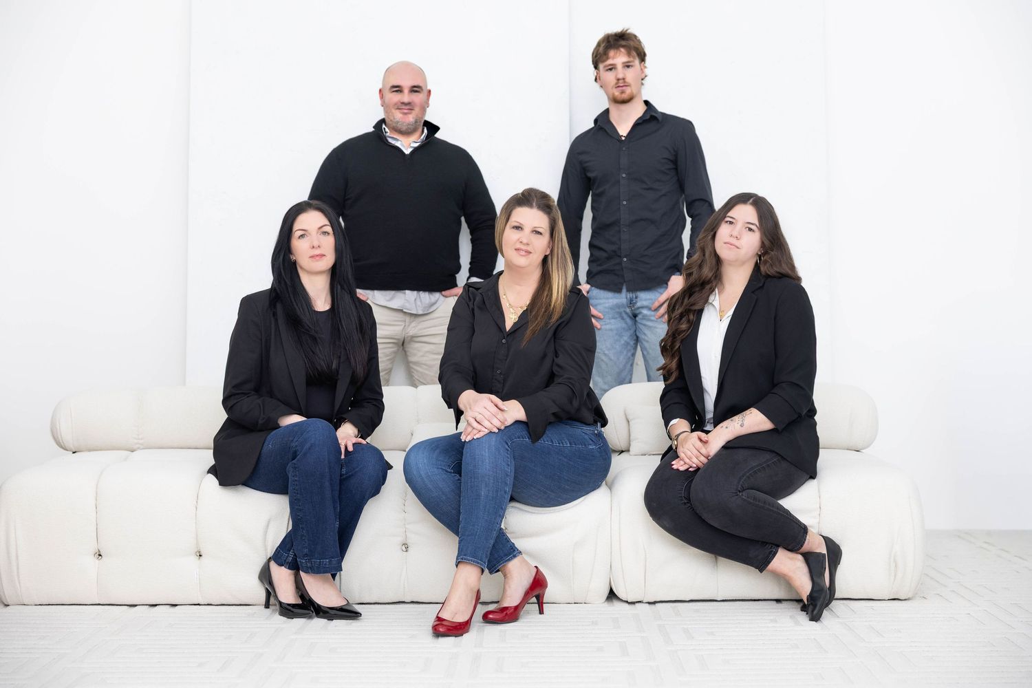 Group of people in coordinated black and navy business attire seated together on white furniture.