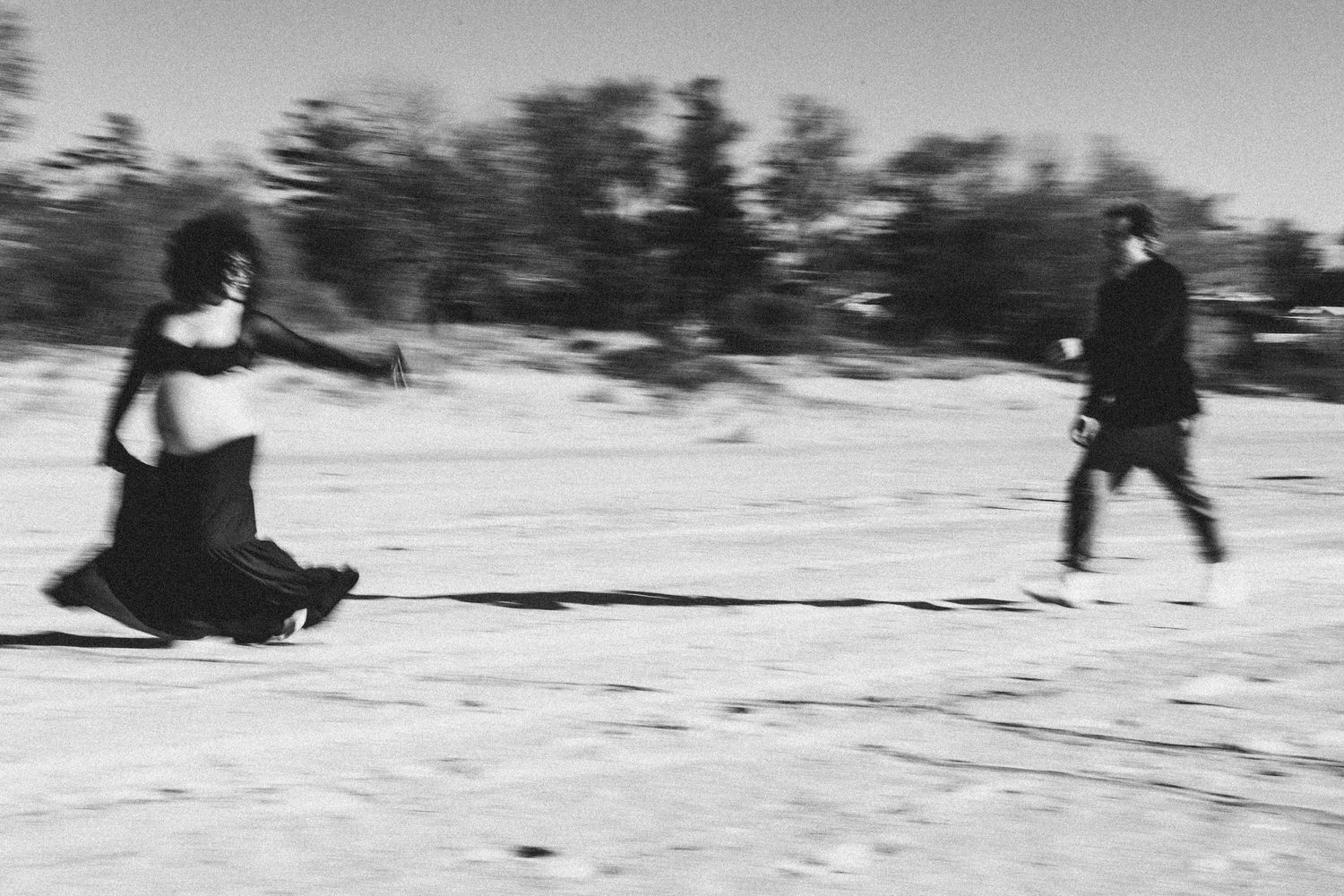 Two people on a snowy winter field, one person skiing while pulling another person on a sled in black and white.