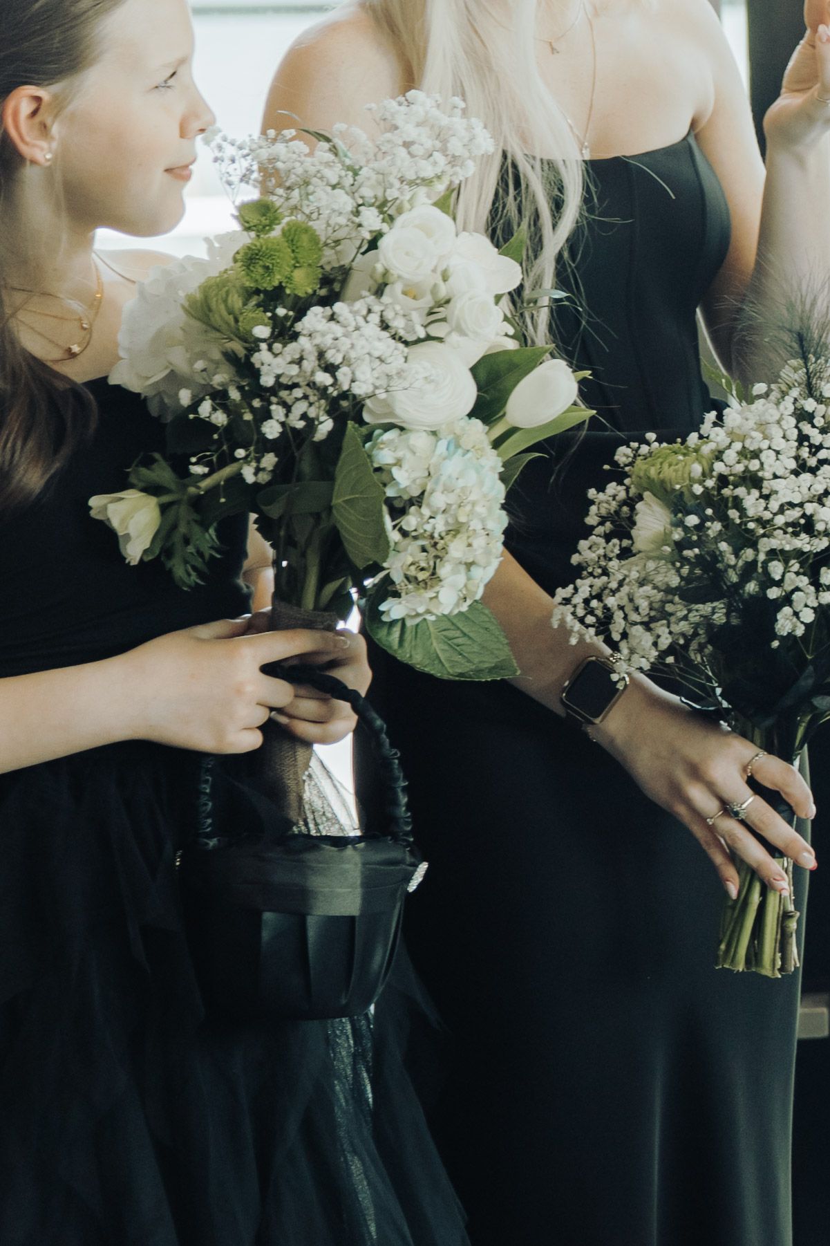 Bridesmaids in black dresses holding white floral bouquets with tulips and baby's breath.