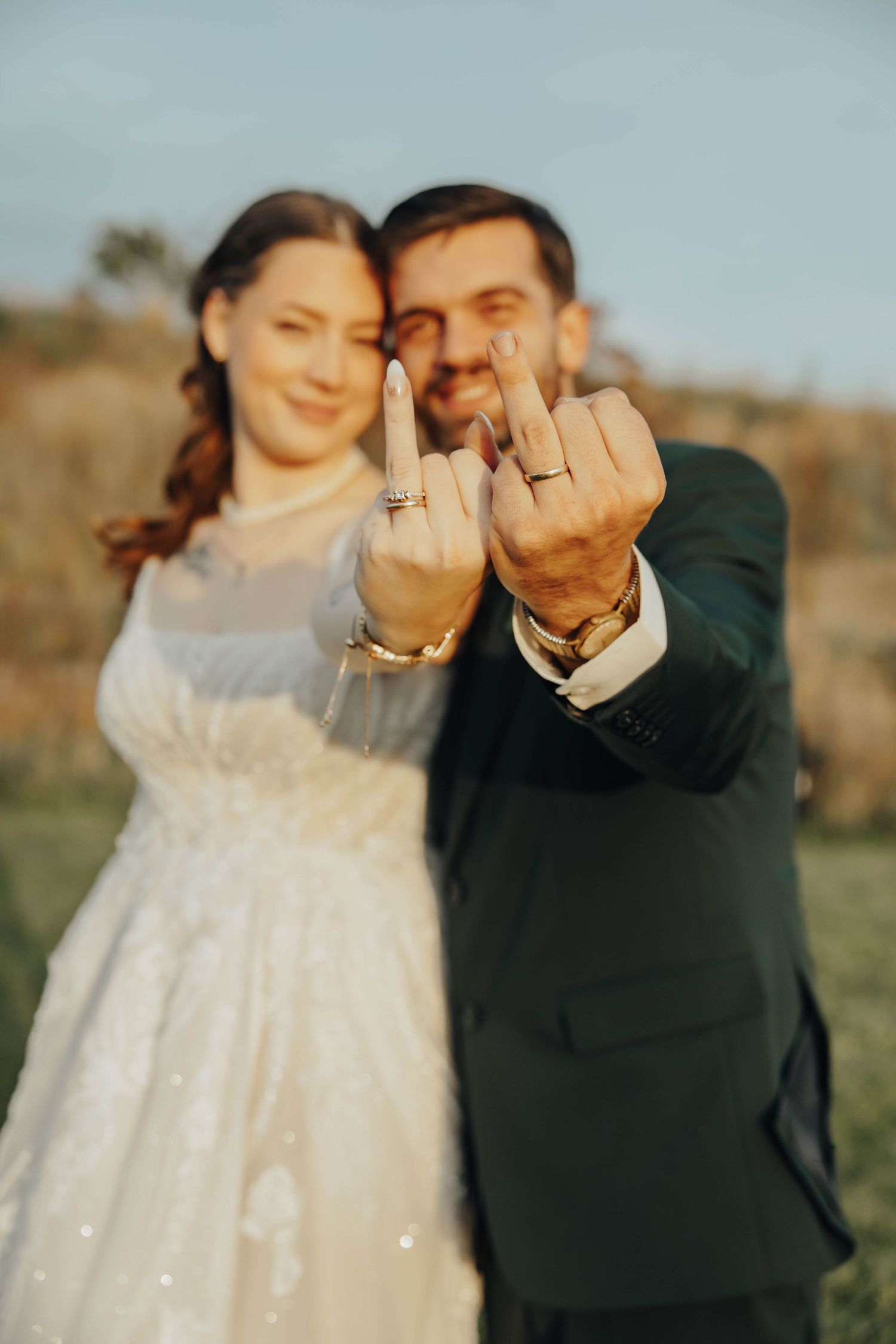 A romantic outdoor wedding photo shoot with a couple showing off their rings in soft natural lighting.