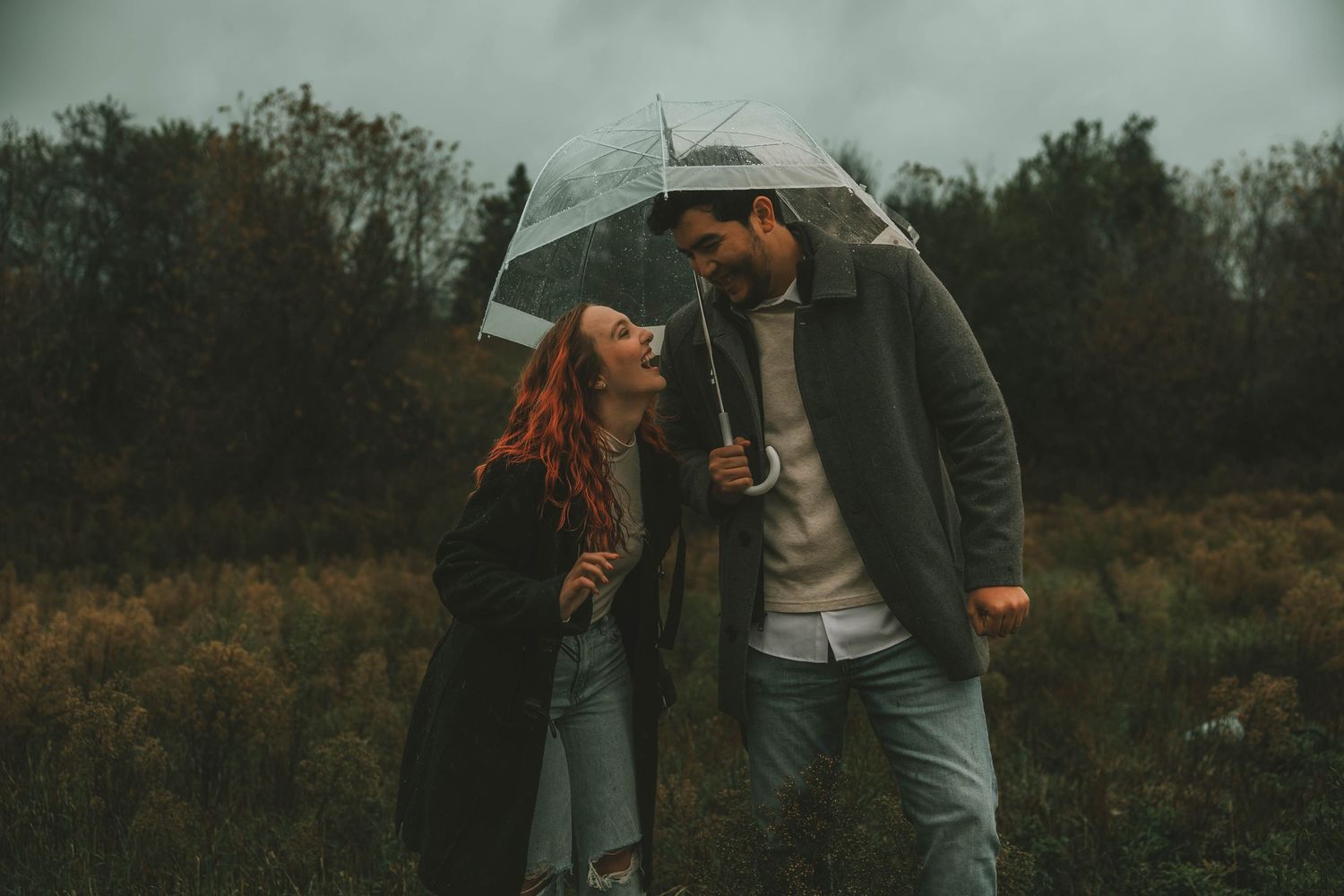 A couple shares a romantic moment under an umbrella in a moody autumn field landscape.