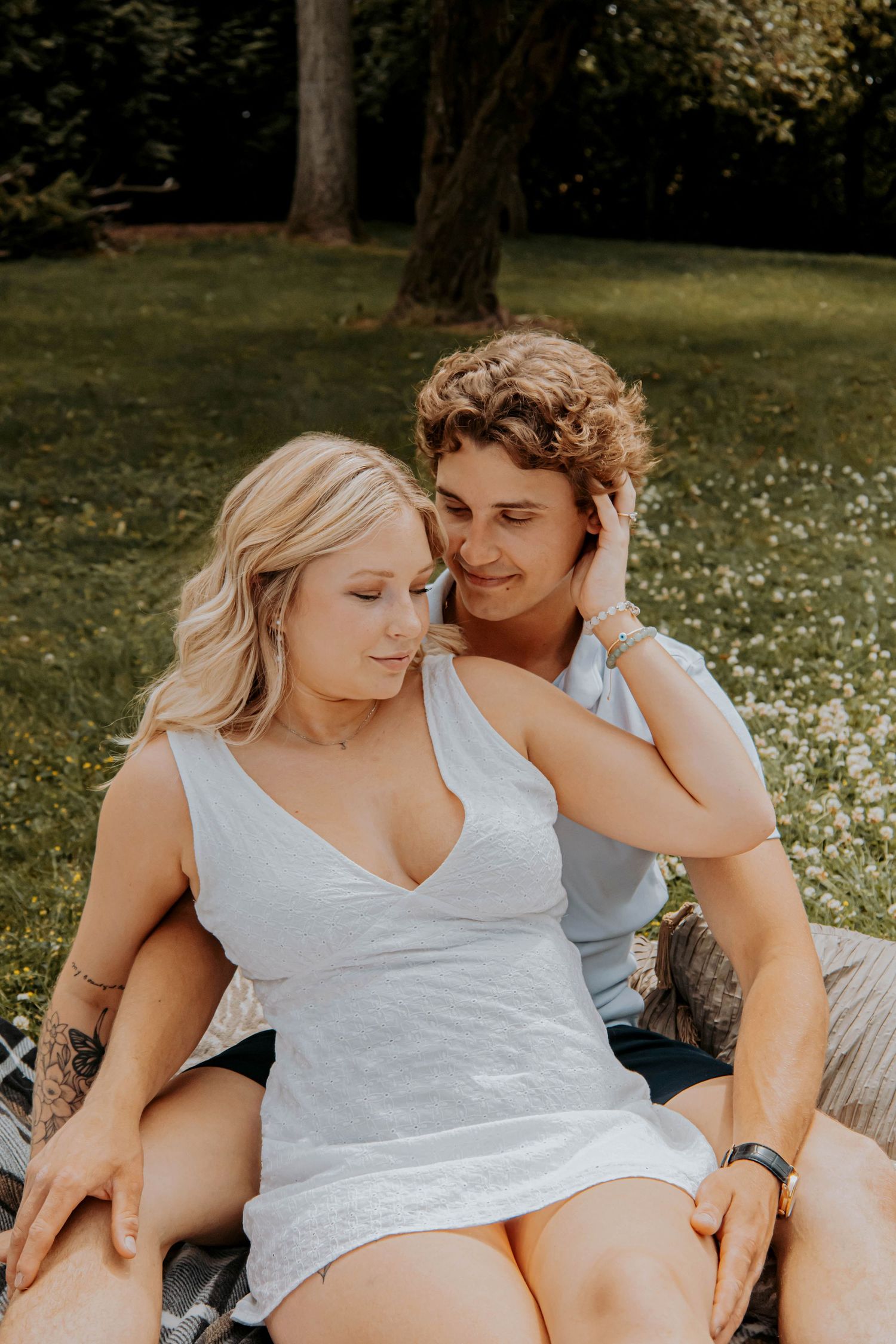 Intimate couple resting on a picnic blanket surrounded by daisies in a park setting.