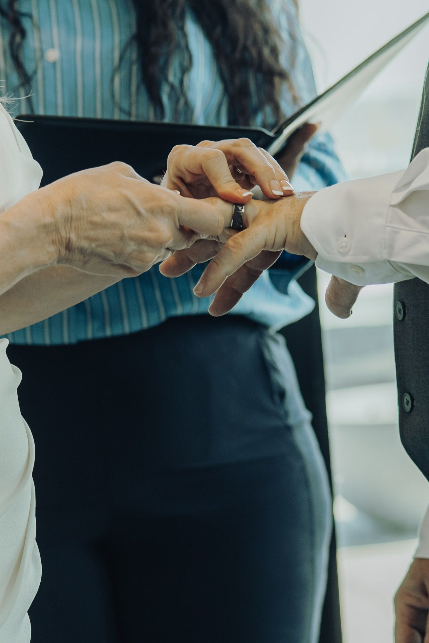 Close-up of a wedding ring exchange ceremony between two people with an officiant holding a book.
