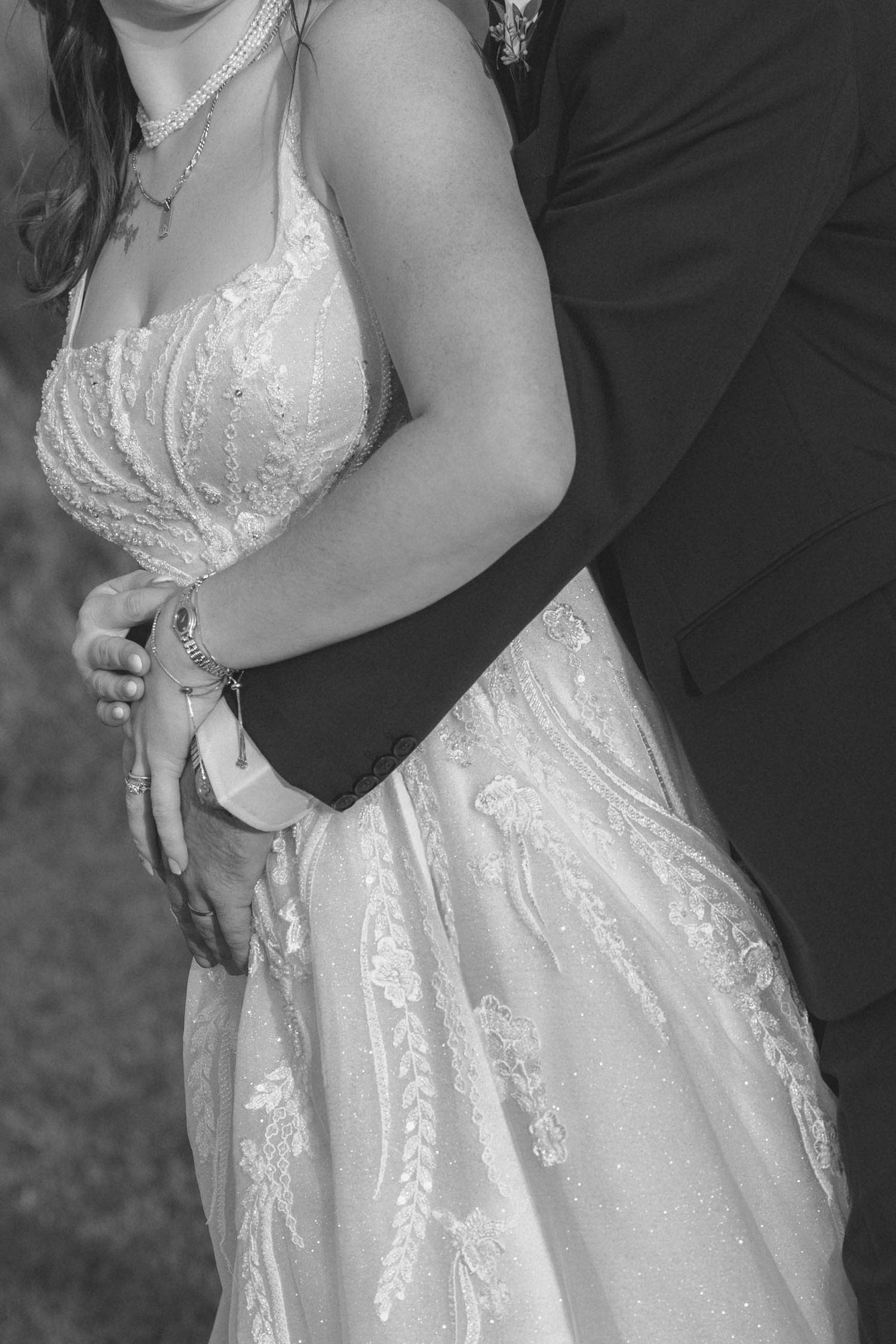 Close-up view of a white lace wedding dress with intricate details as couple embraces during romantic moment.