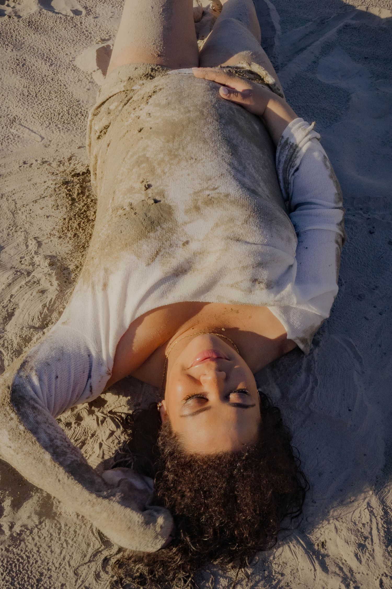 A relaxed beach portrait with someone lying on sand during golden hour.