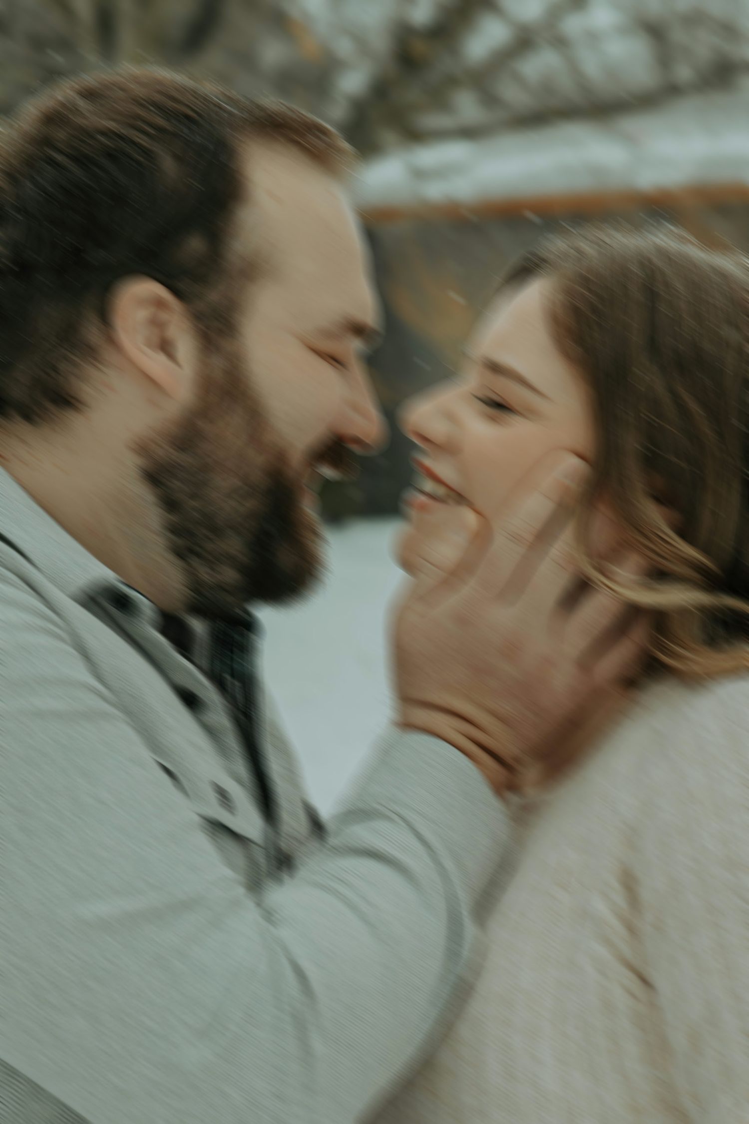 A romantic winter engagement photo showing a tender moment between a couple laughing and touching faces outdoors.