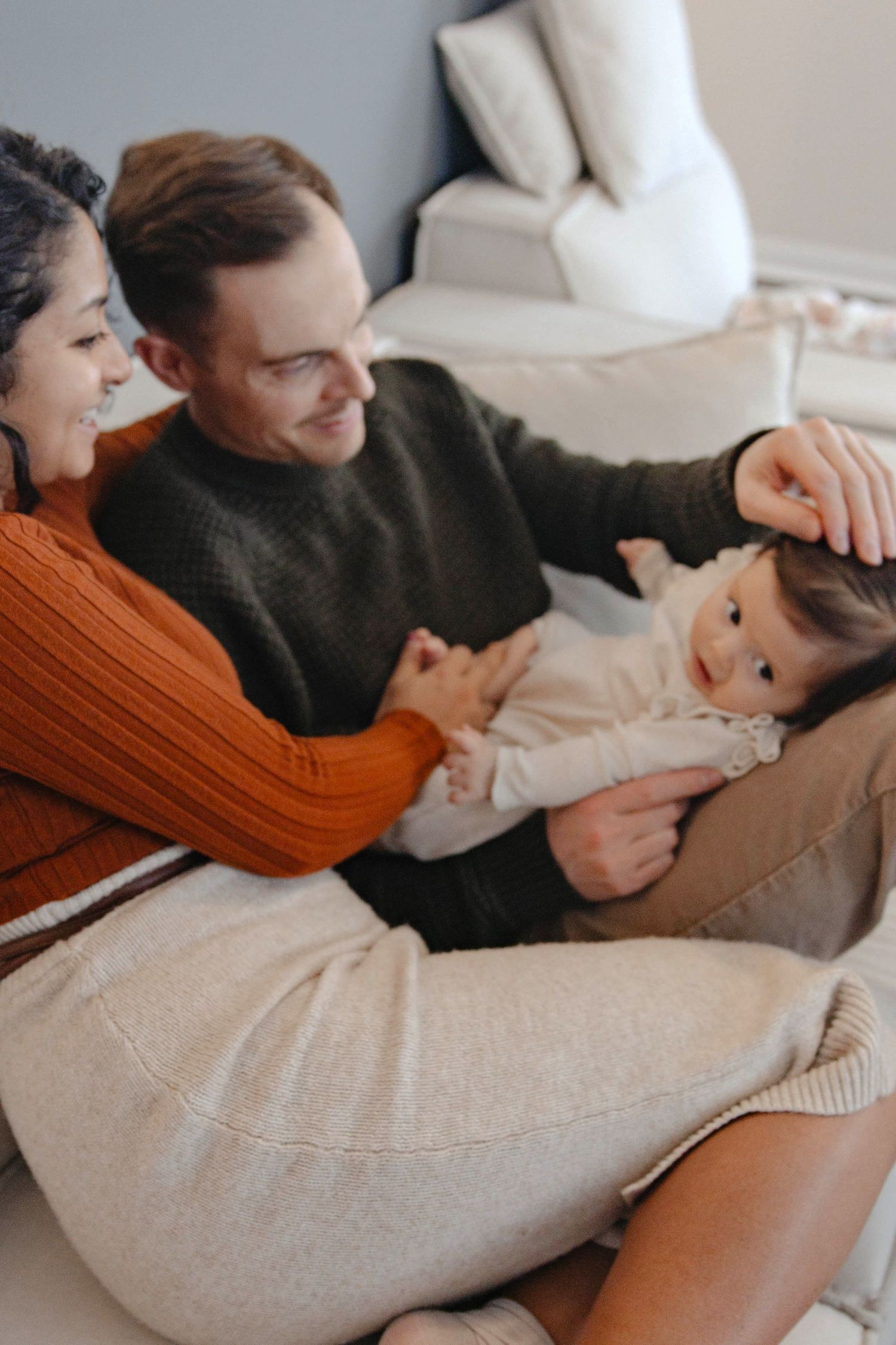 A loving family moment on a cozy couch as they cuddle and play together in warm autumn-colored sweaters.