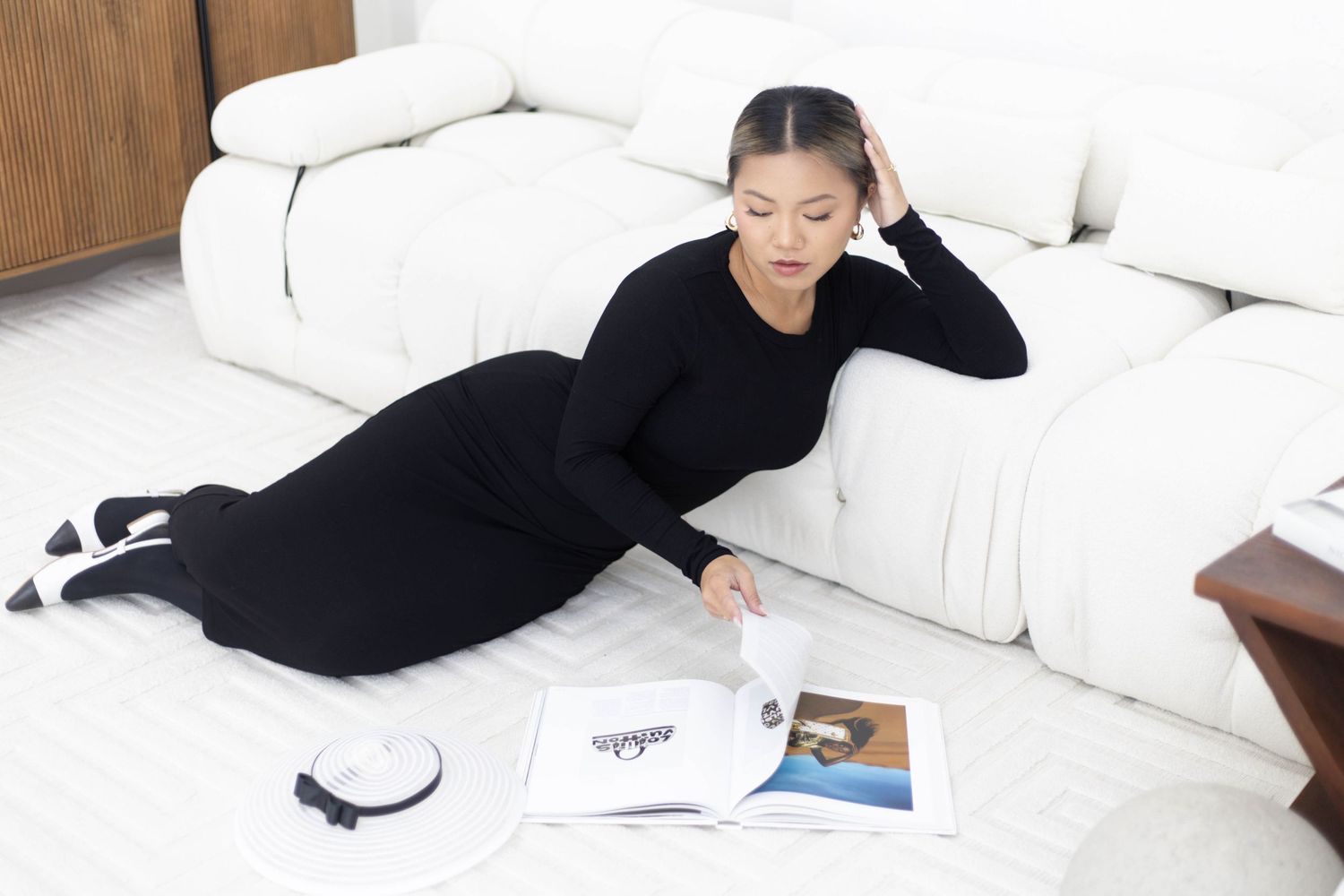 Person in black loungewear relaxes on a white couch while looking at magazines.
